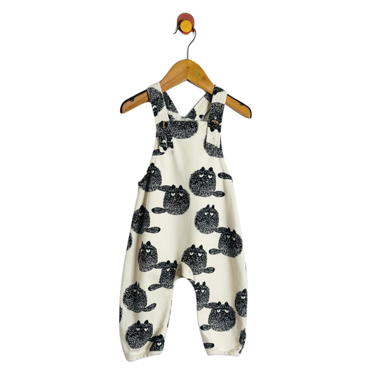 A baby romper in cream fabric with a black cat pattern, hanging on a wooden hanger against a plain white background.