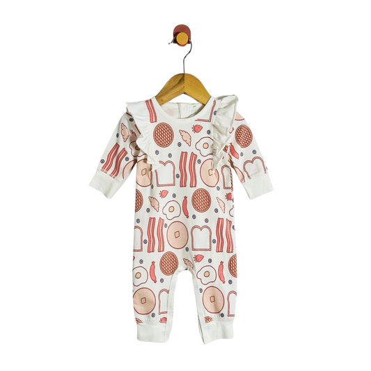 A baby long-sleeve footless romper hanging on a wooden hanger against a plain white background. The romper is off-white with a colorful breakfast food print featuring eggs, bacon, toast, and pancakes.