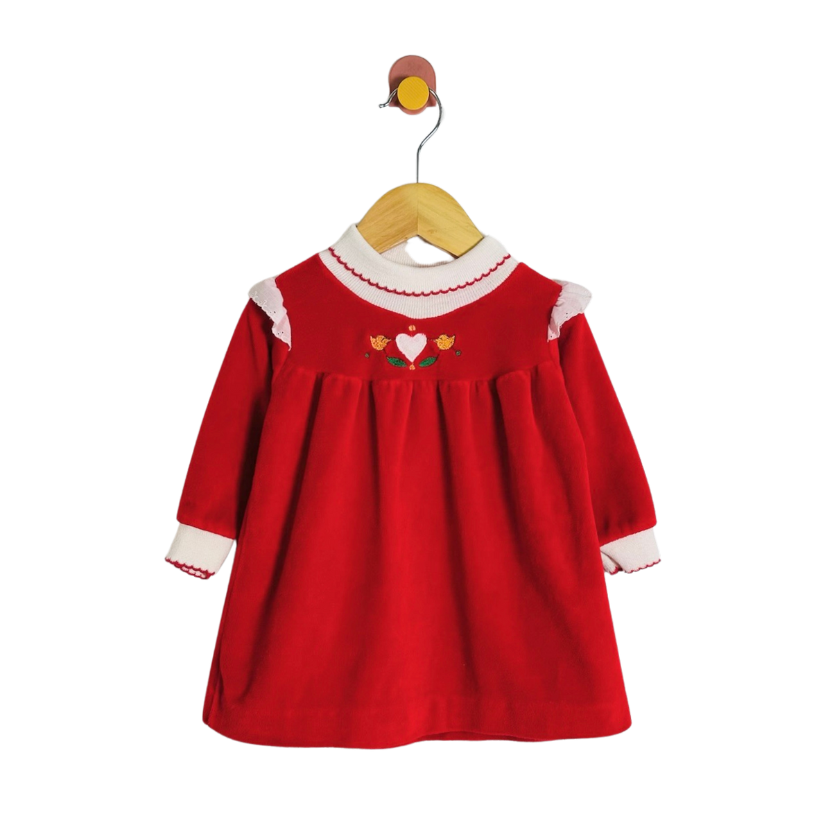 A red long-sleeve baby dress with white ruffled trim at the collar and cuffs, featuring a small embroidered heart and flowers on the chest, hanging on a wooden hanger against a white background.