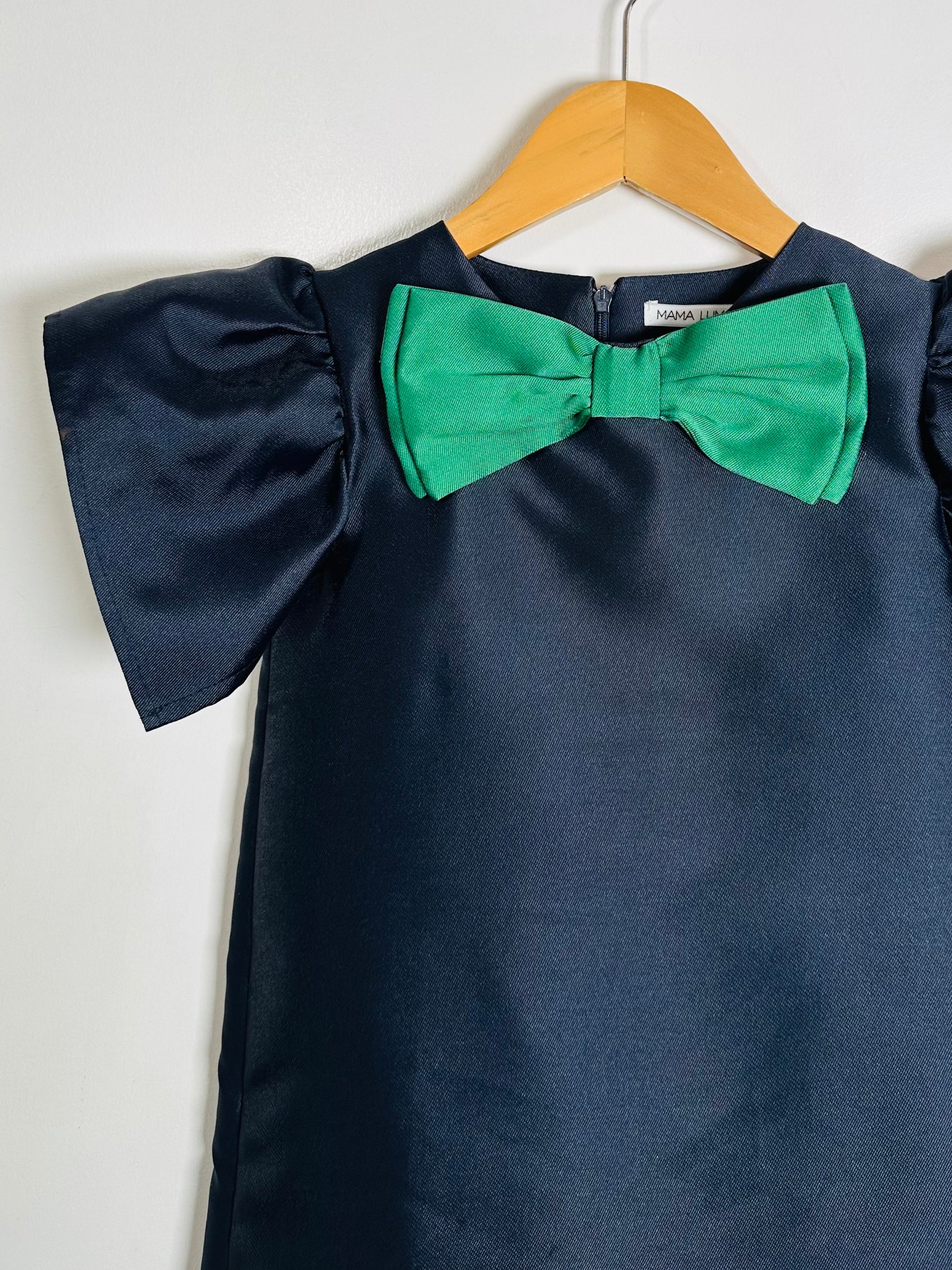 Navy blue dress with a green bow on a hanger against a white background