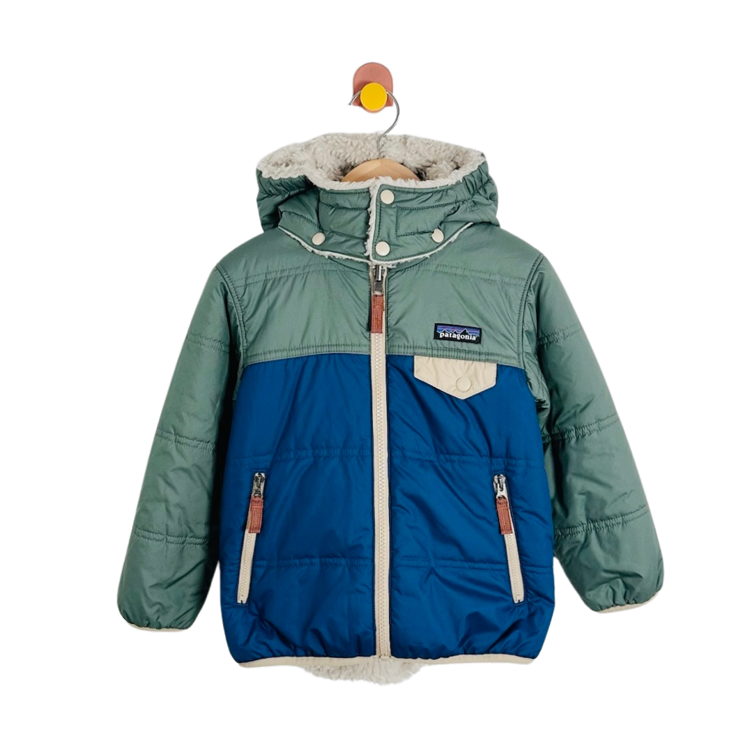 A Patagonia kids' puffer jacket in sage green and blue, featuring a hood, faux-fur lining, and a front zipper, shown hanging on a wooden hanger against a white background.