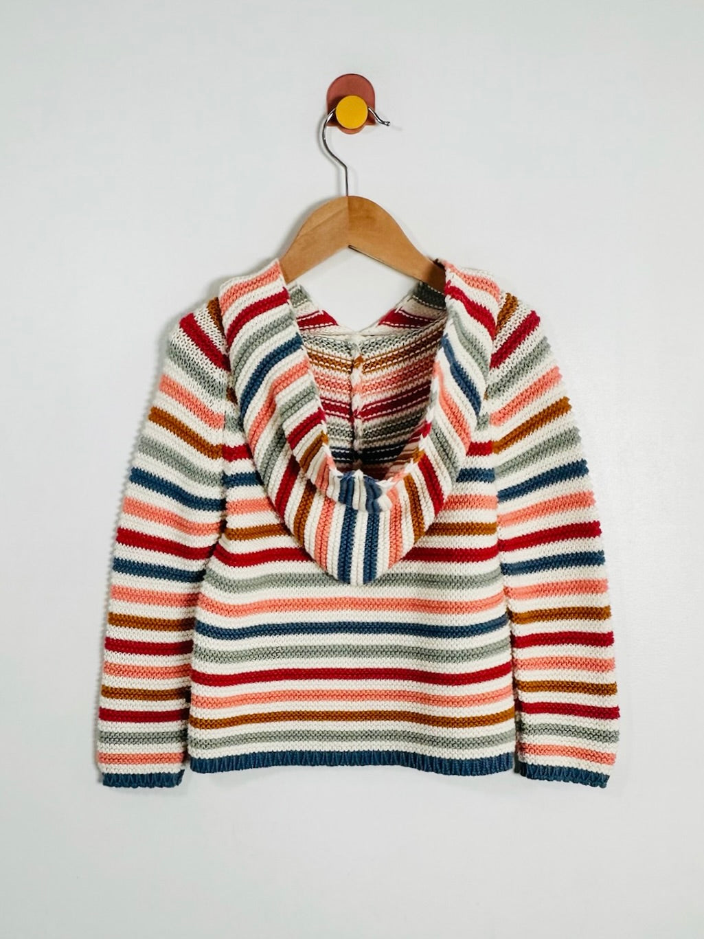 A striped knit sweater with a wide cowl neck, hanging on a wooden hanger against a plain light gray wall.