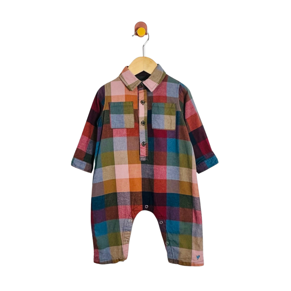 A baby romper with a colorful plaid pattern, featuring a button-down shirt collar and three-quarter sleeves, hanging on a wooden hanger against a white background.