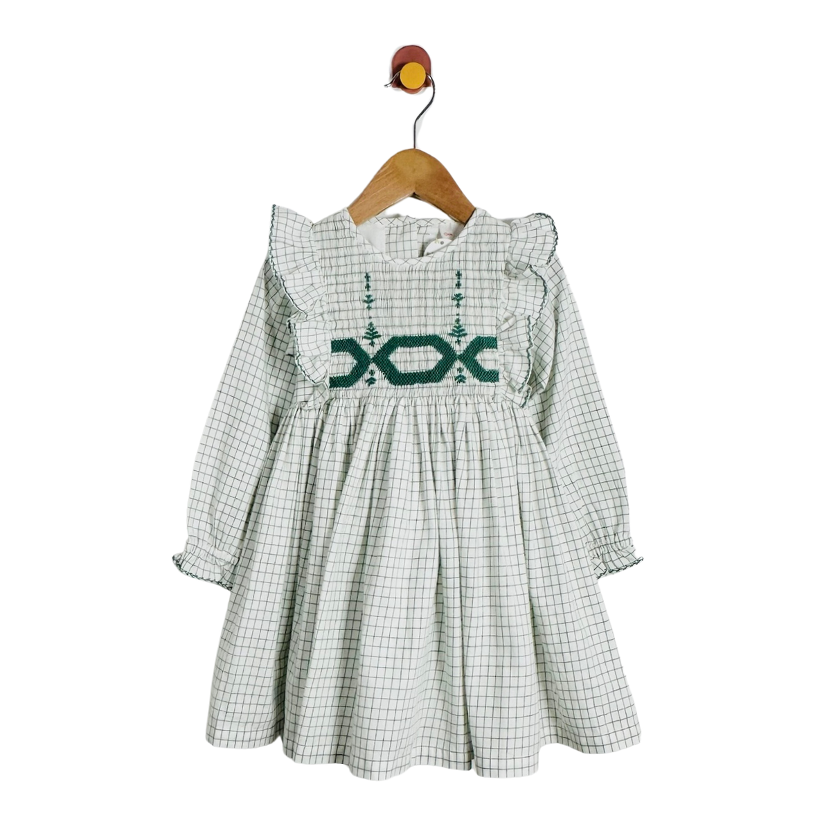 A long-sleeve baby dress with a green and white gingham pattern, featuring a dark green embroidered geometric design across the chest and ruffled shoulders, hanging on a wooden hanger against a white background.