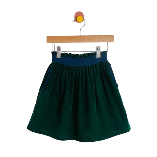 A dark green corduroy skirt with a navy blue elastic waistband, hanging from a wooden hanger with metal clips against a plain white background.