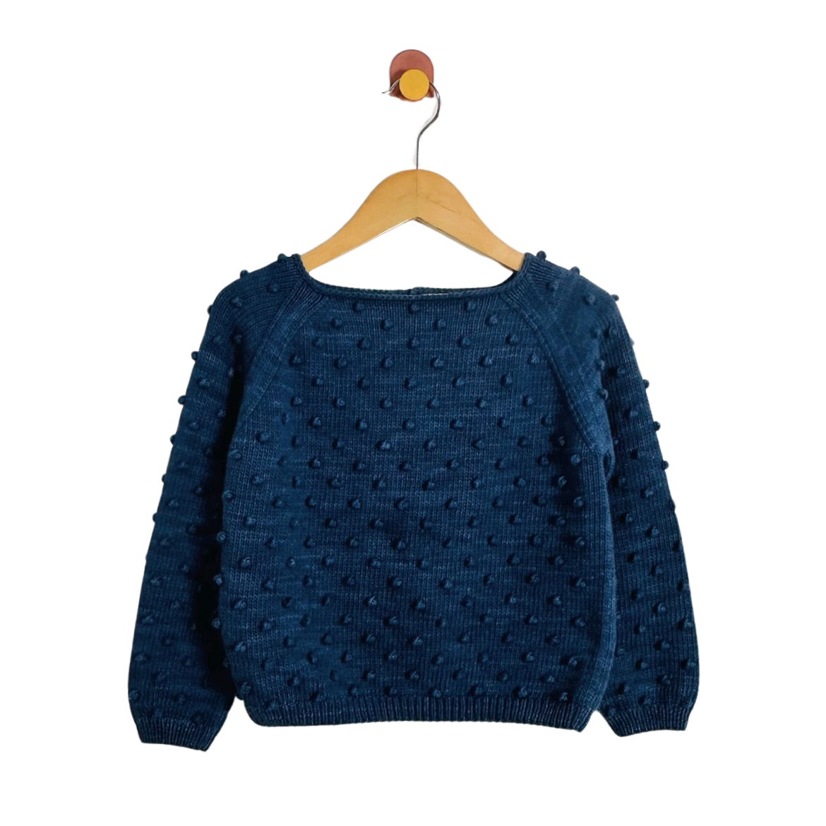A dark blue textured knit sweater with raised pom-pom details, hanging on a wooden hanger against a plain white background.