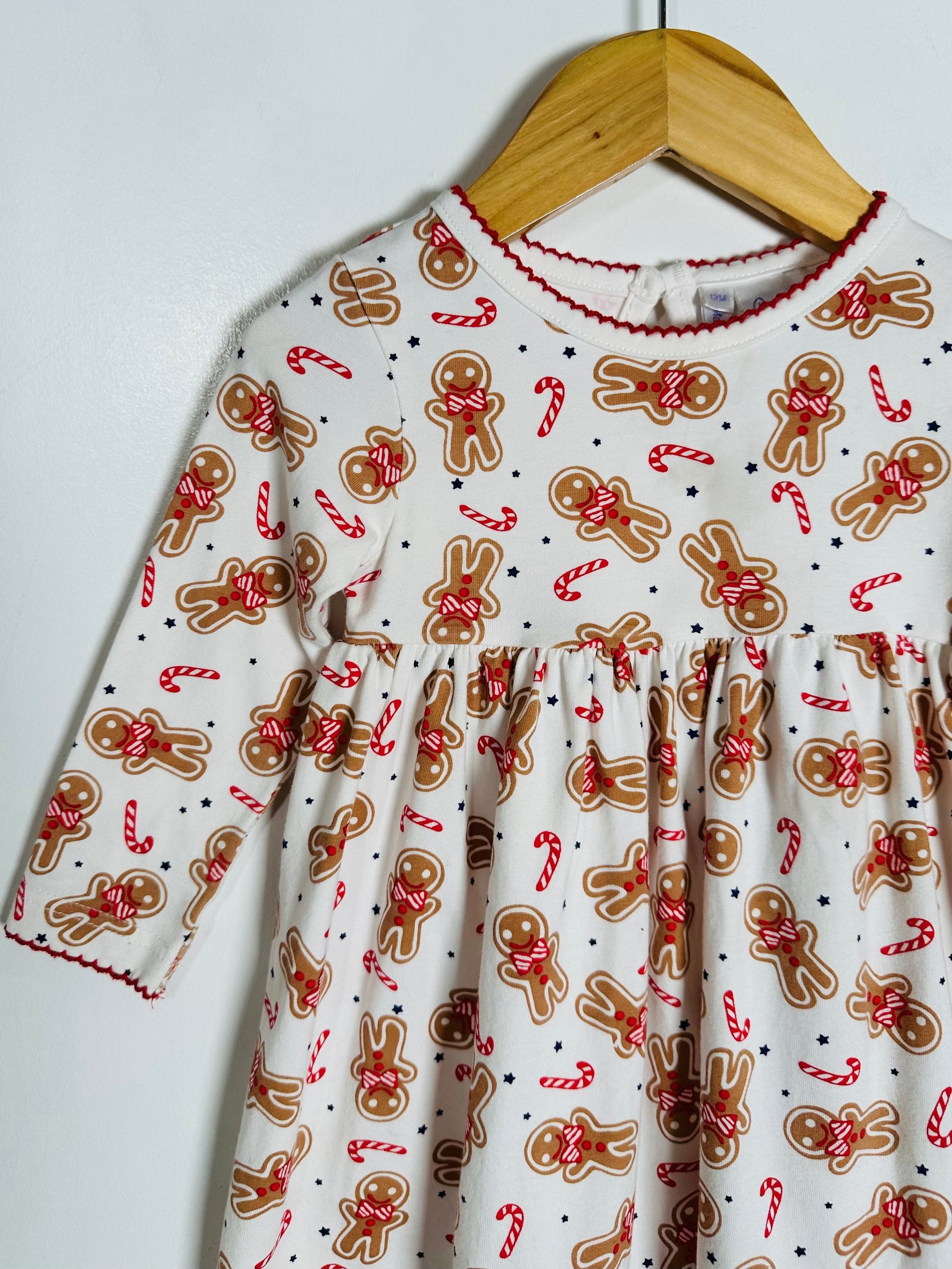 Children's dress with gingerbread man and candy cane pattern on a hanger against a white background