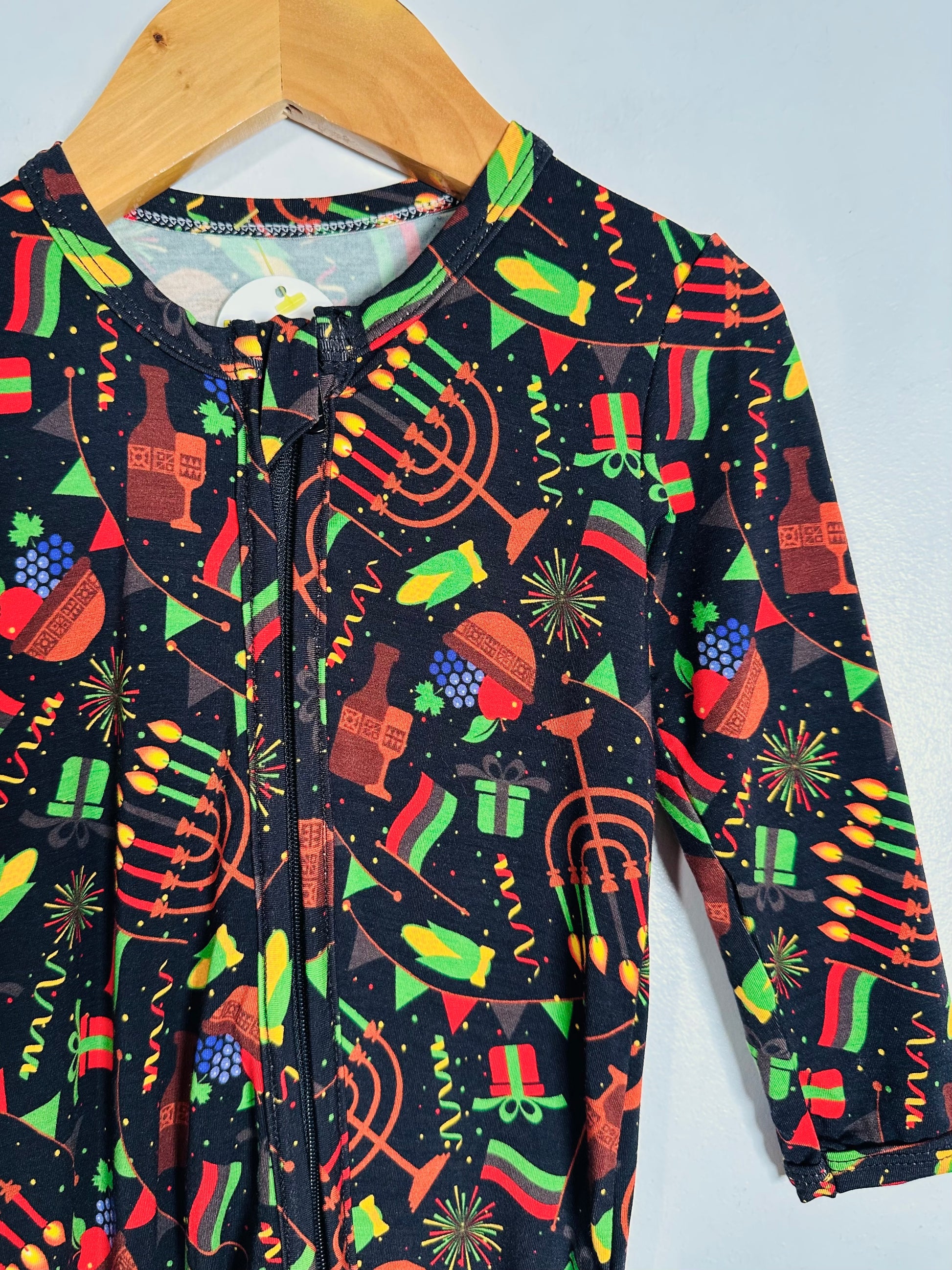 Children's onesie with festive pattern on a hanger against a light gray background