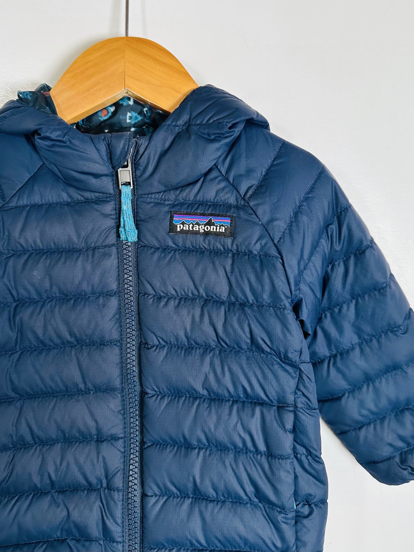 Blue puffer jacket with Patagonia logo on a hanger against a white background