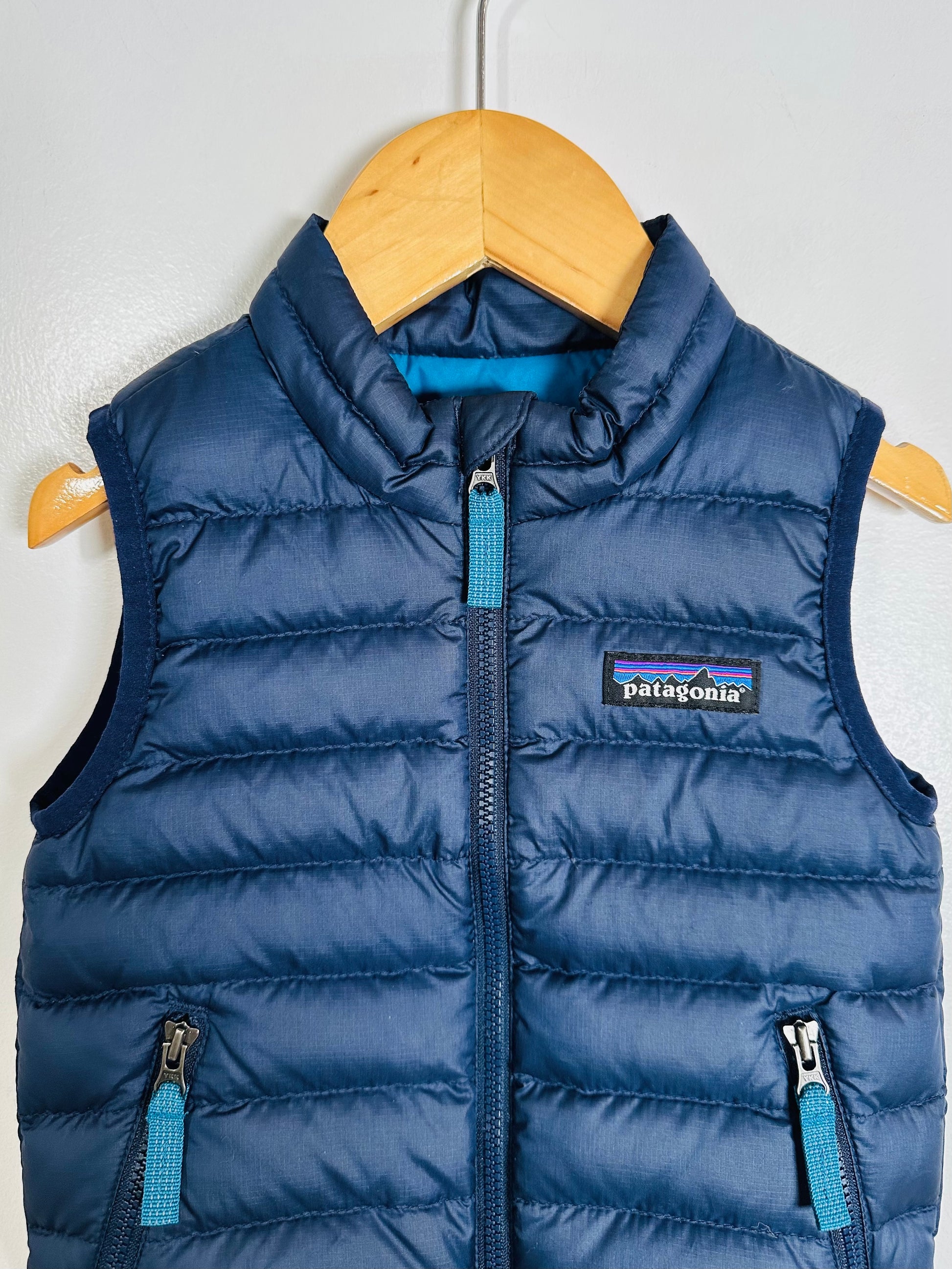 Blue puffer vest with Patagonia logo on a wooden hanger against a white background