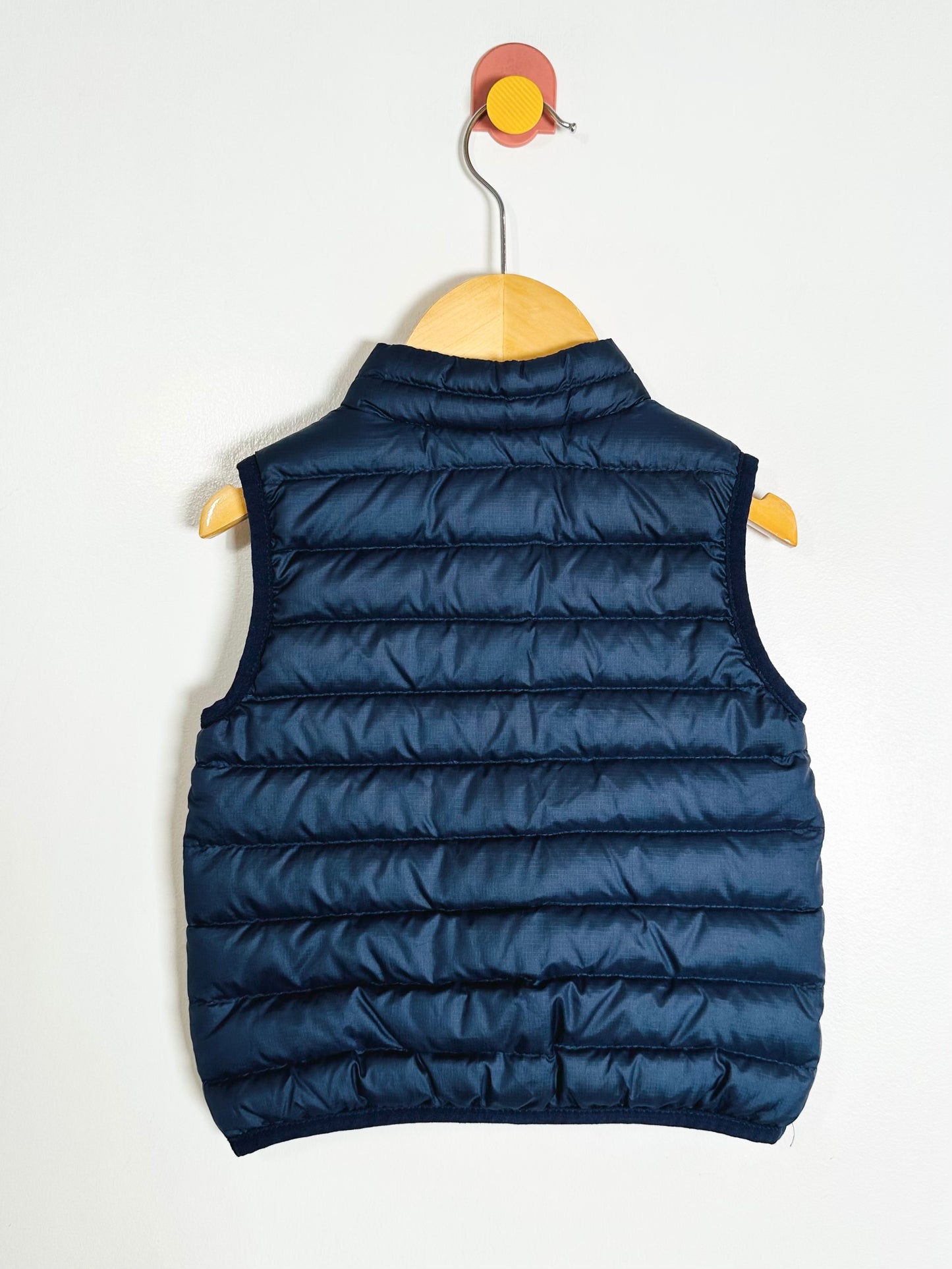 Blue puffer vest on a wooden hanger against a white background