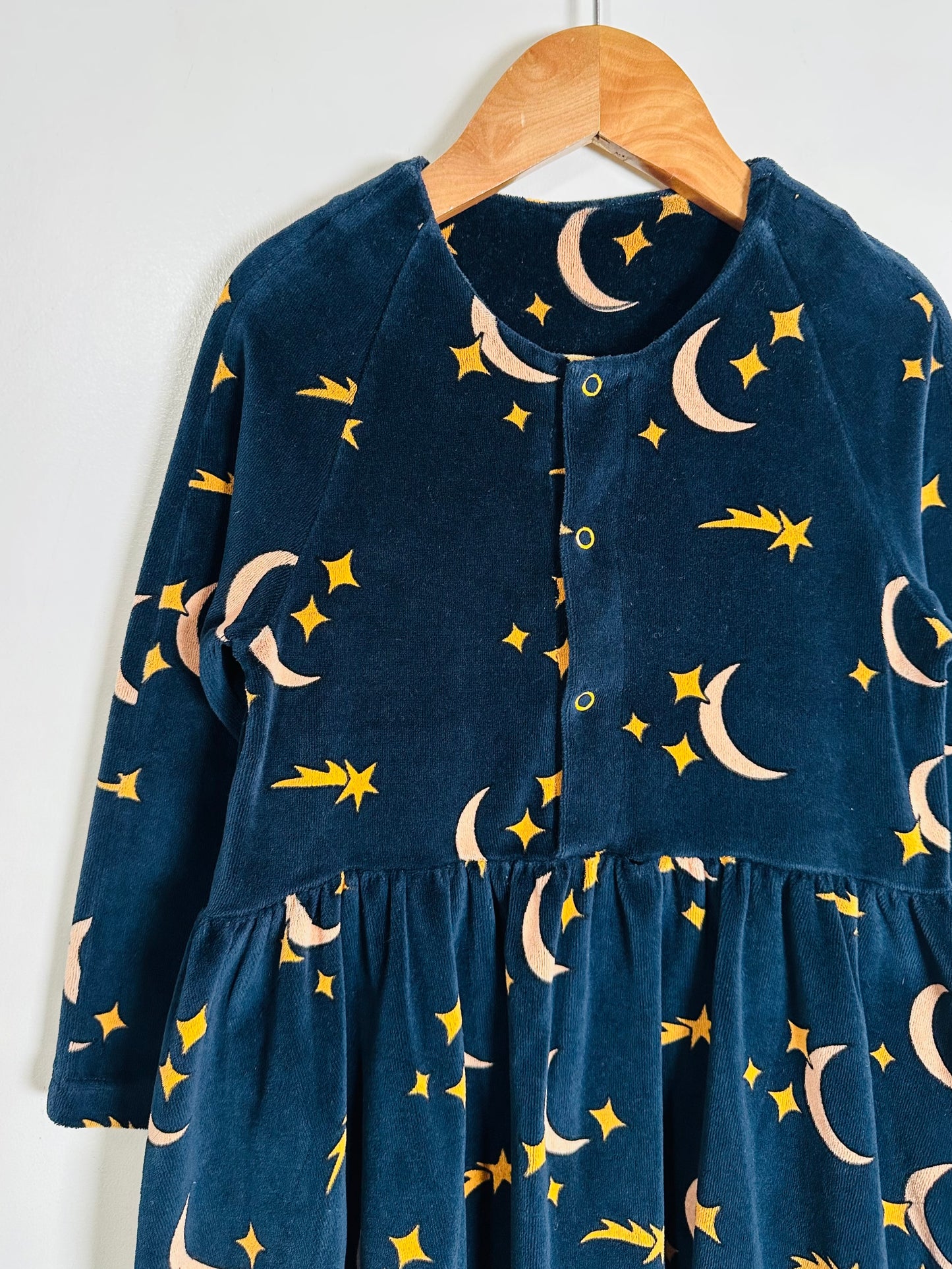 Navy blue dress with celestial pattern on a wooden hanger against a white background