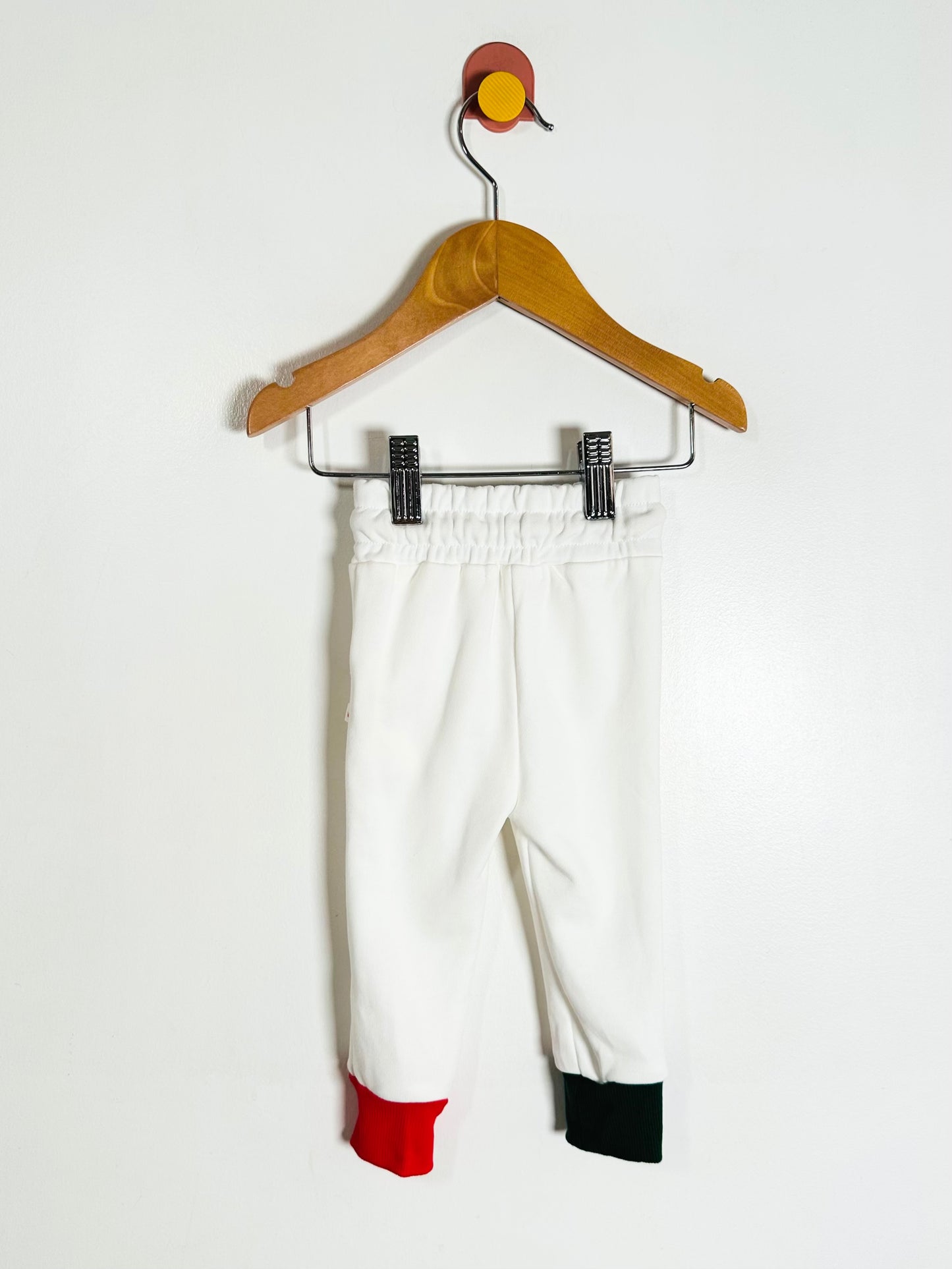 White pants with red and green accents on a hanger against a white background