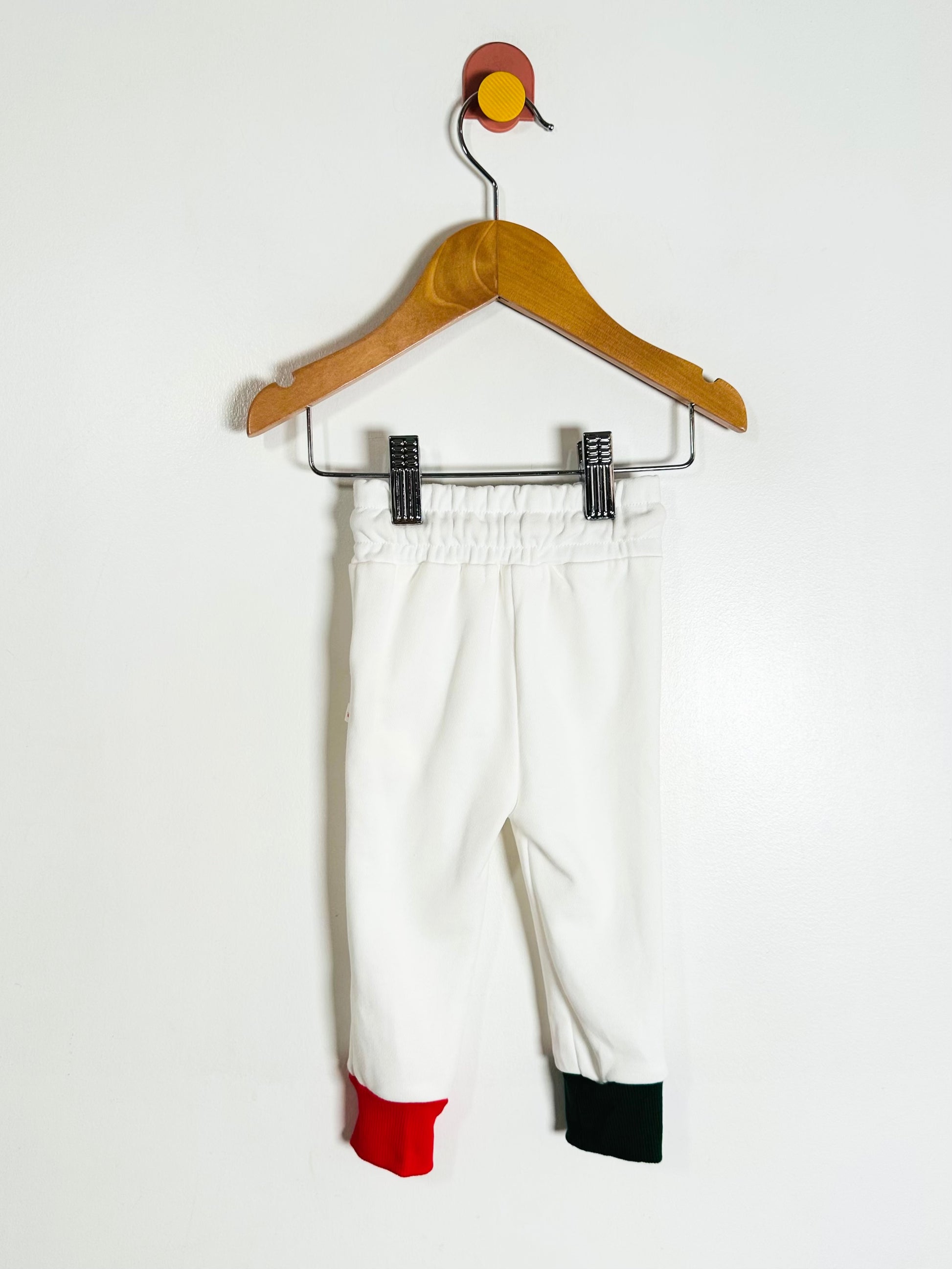 White pants with red and green accents on a hanger against a white background