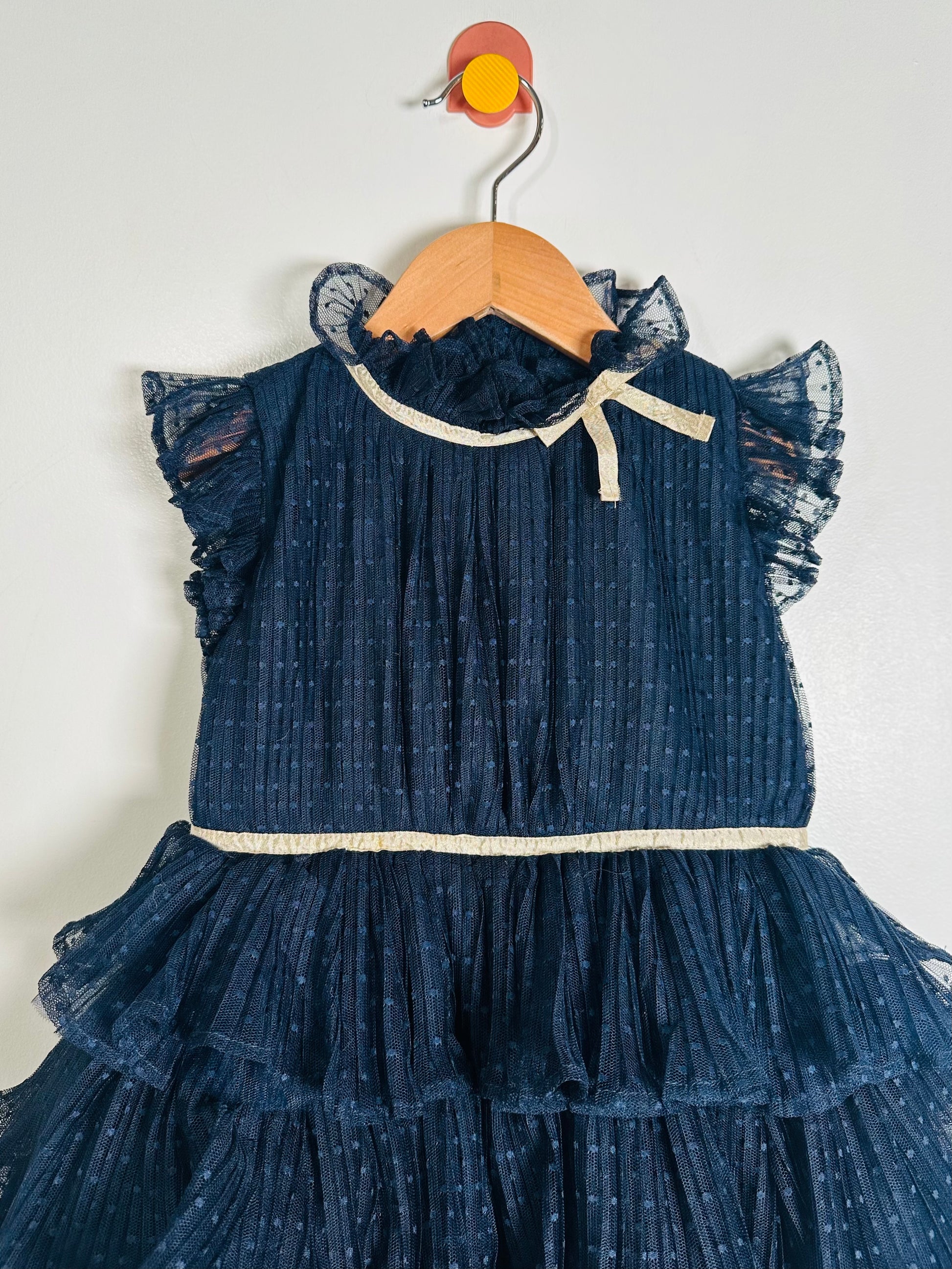 Blue ruffled dress on a wooden hanger against a white background