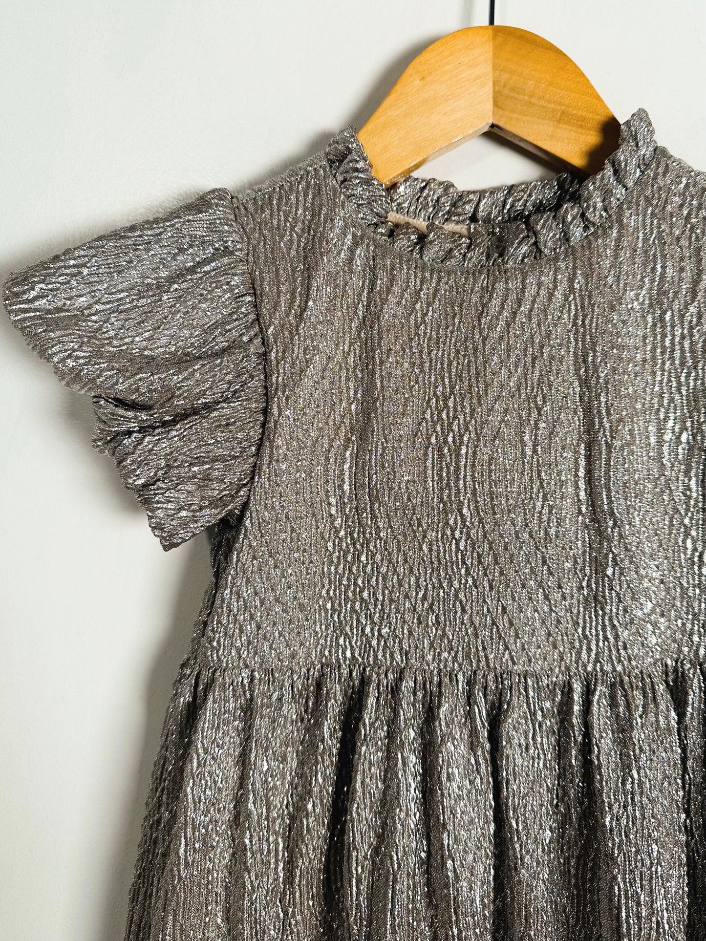 Silver metallic dress on a wooden hanger against a white background