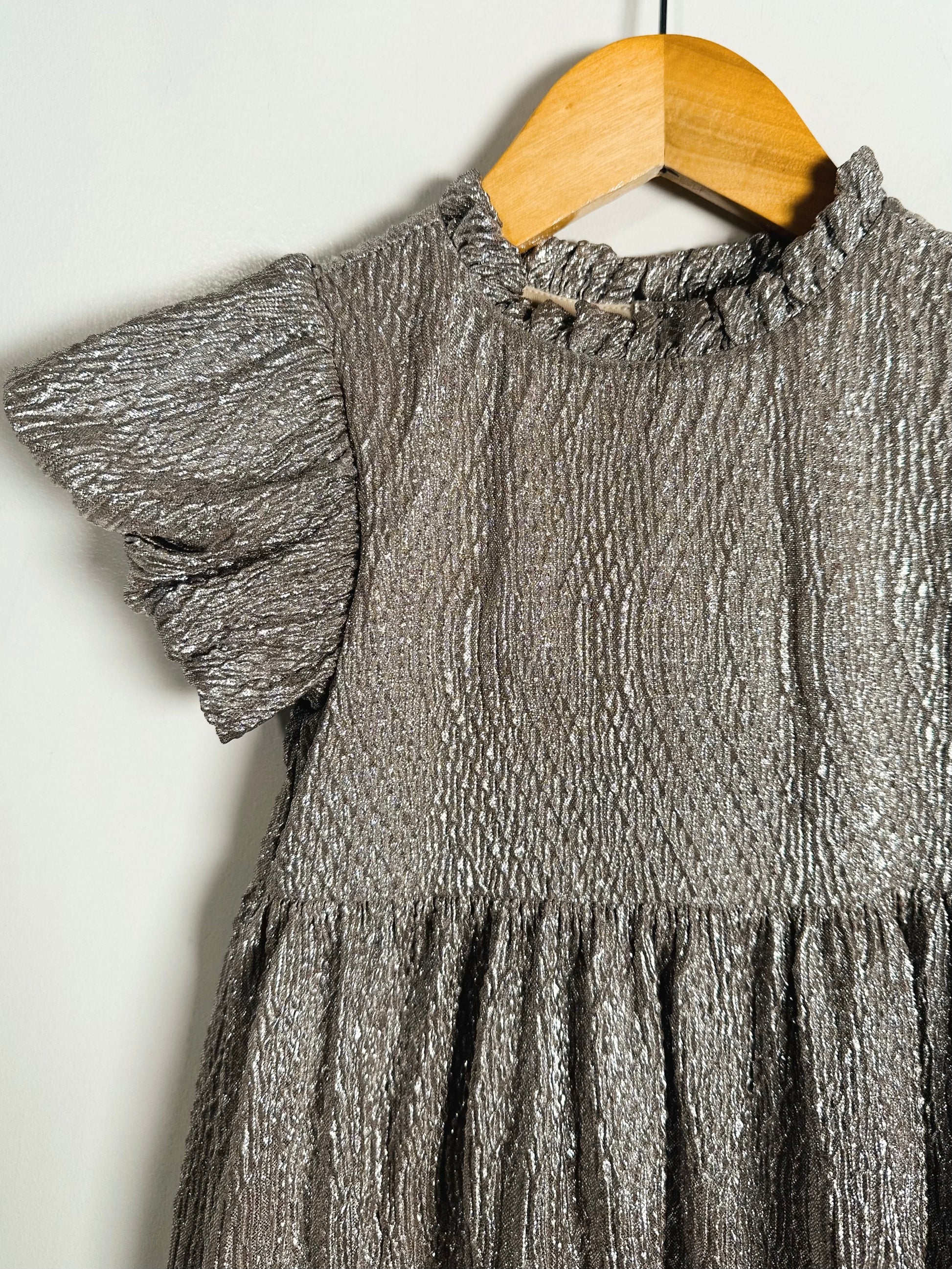 Silver metallic dress on a wooden hanger against a white background