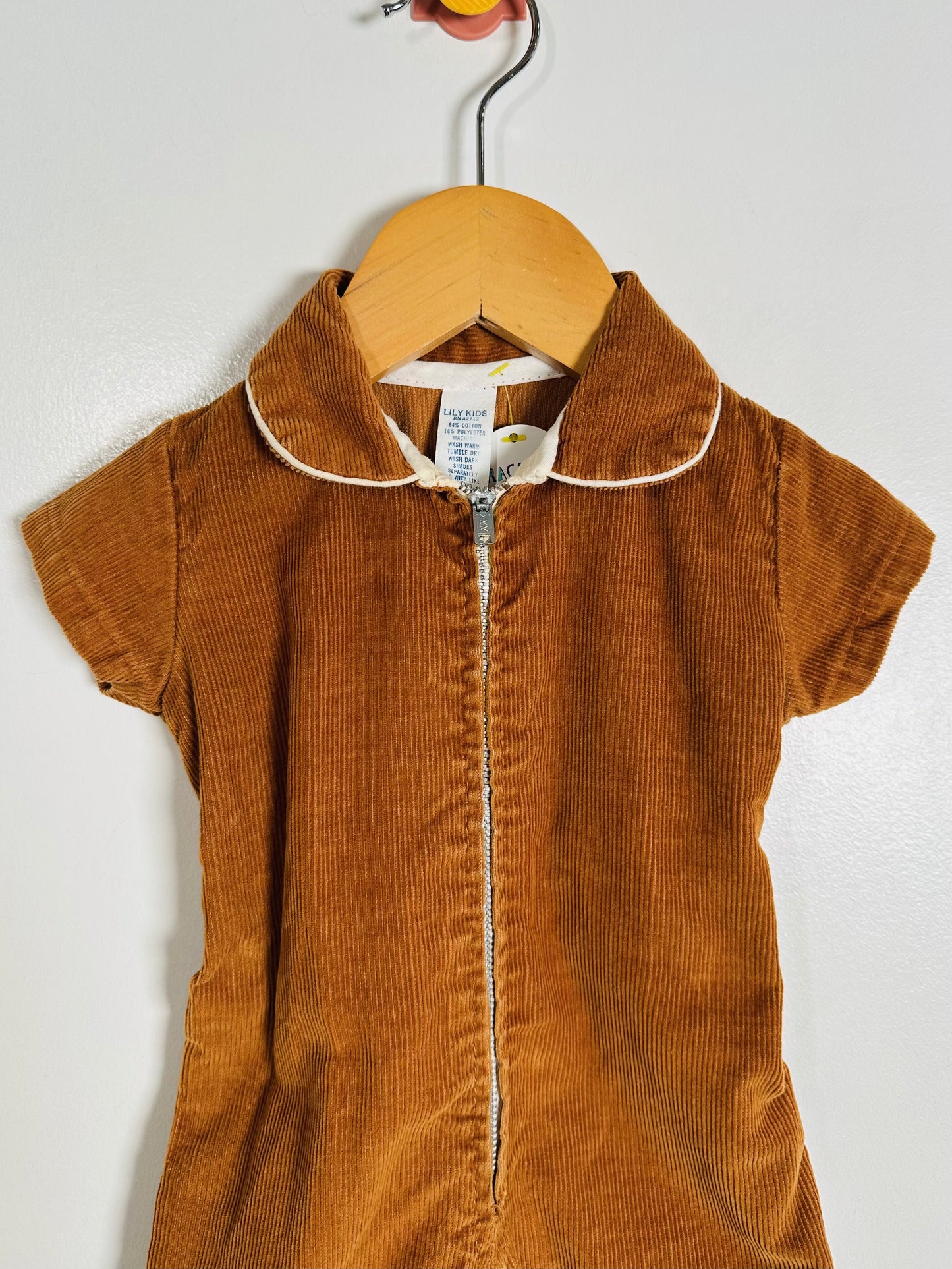 Brown corduroy dress with white trim on a hanger against a white background