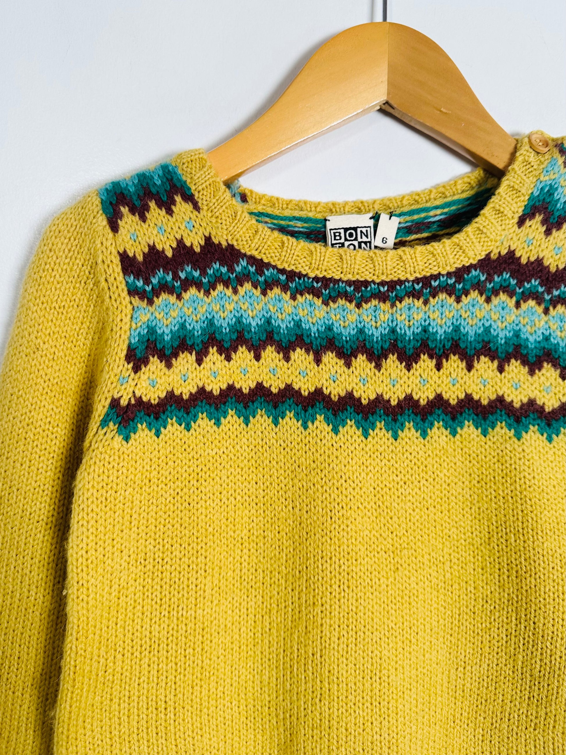 Yellow sweater with patterned collar on a hanger against a white wall