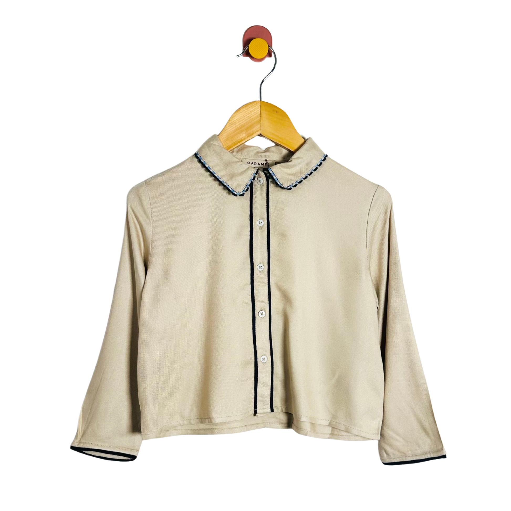 Beige shirt with trim on a wooden hanger against a white background