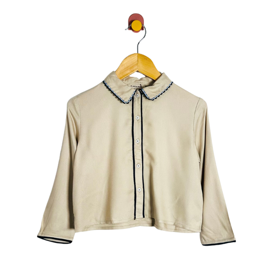Beige shirt with trim on a wooden hanger against a white background