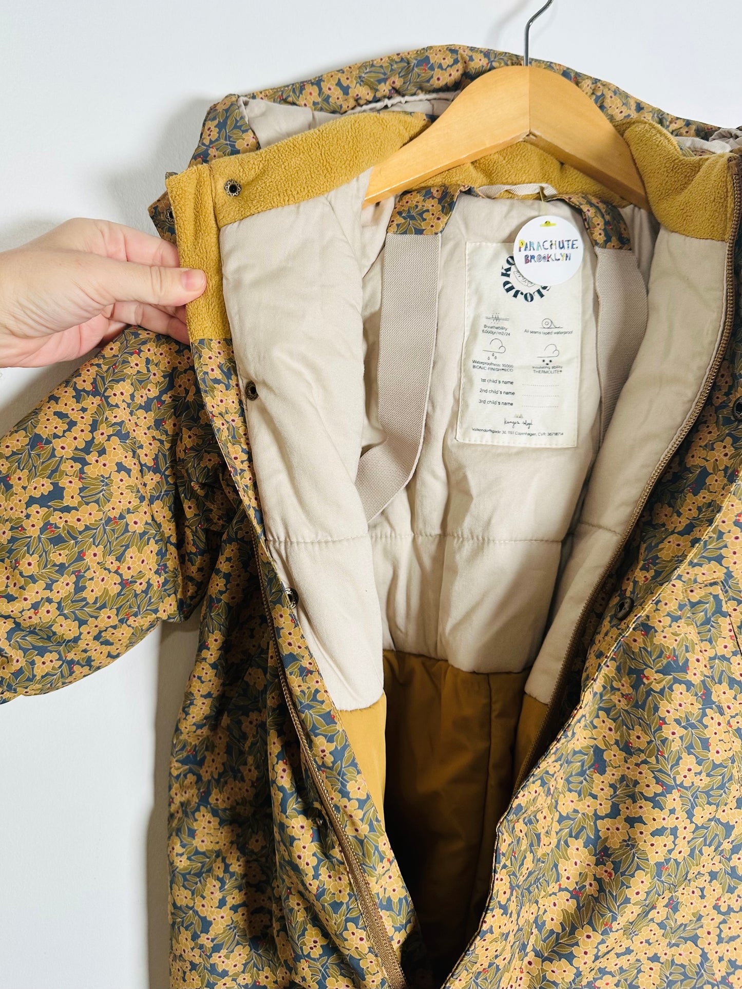 Floral-patterned snowsuit with beige lining and visible brand label on a hanger.