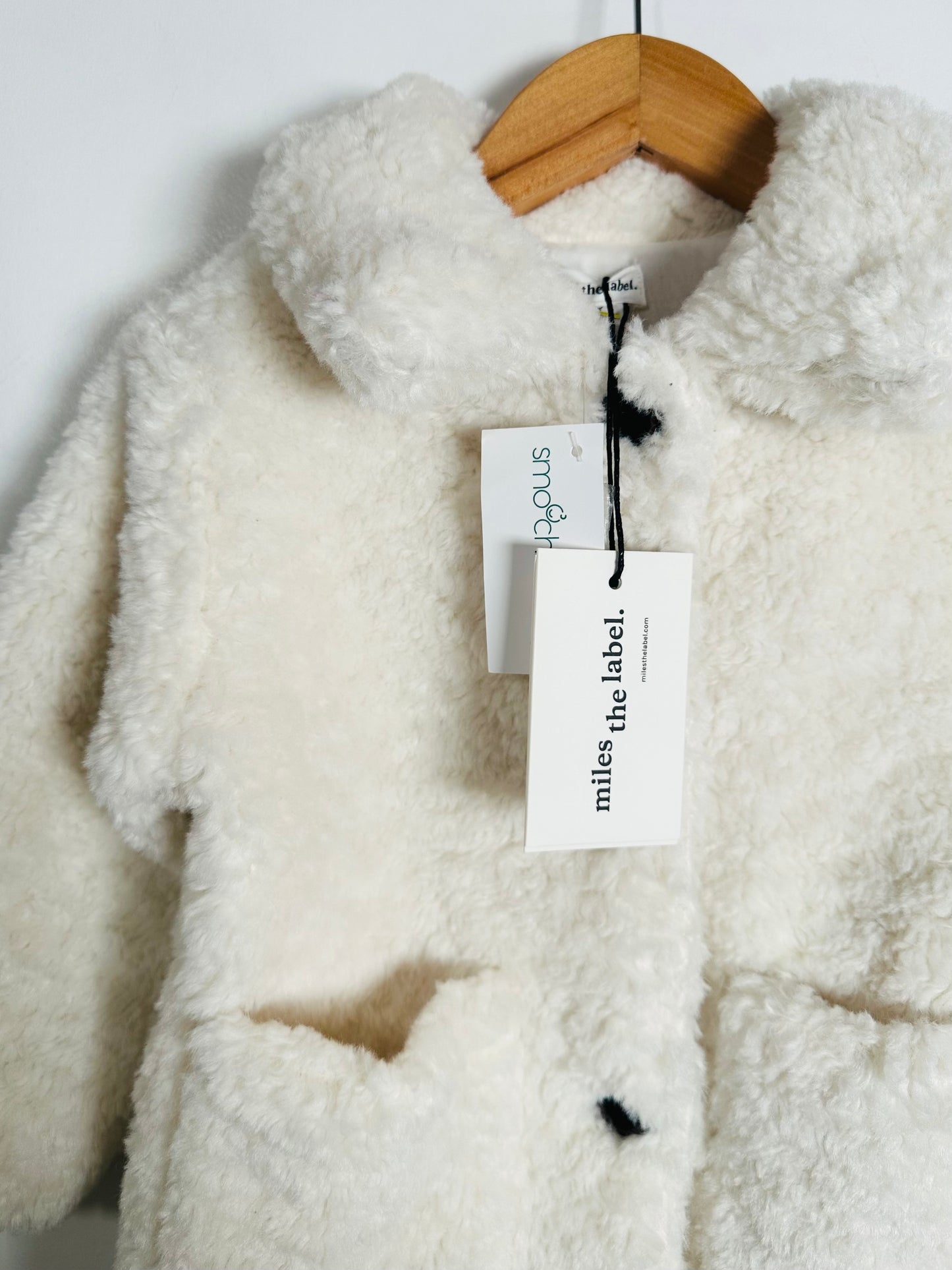 White sherpa jacket on a hanger with 'miles the label' tag.