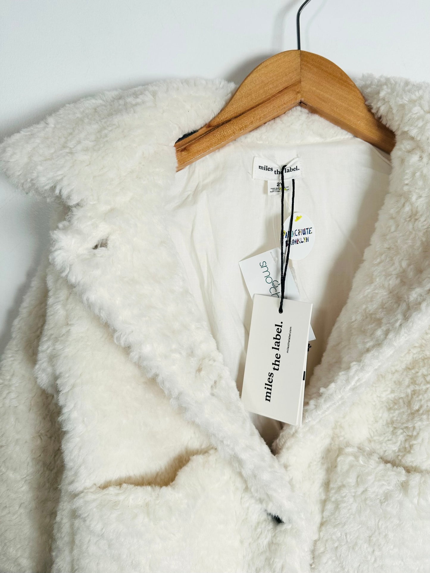White sherpa jacket on a hanger with 'miles the label' tags.