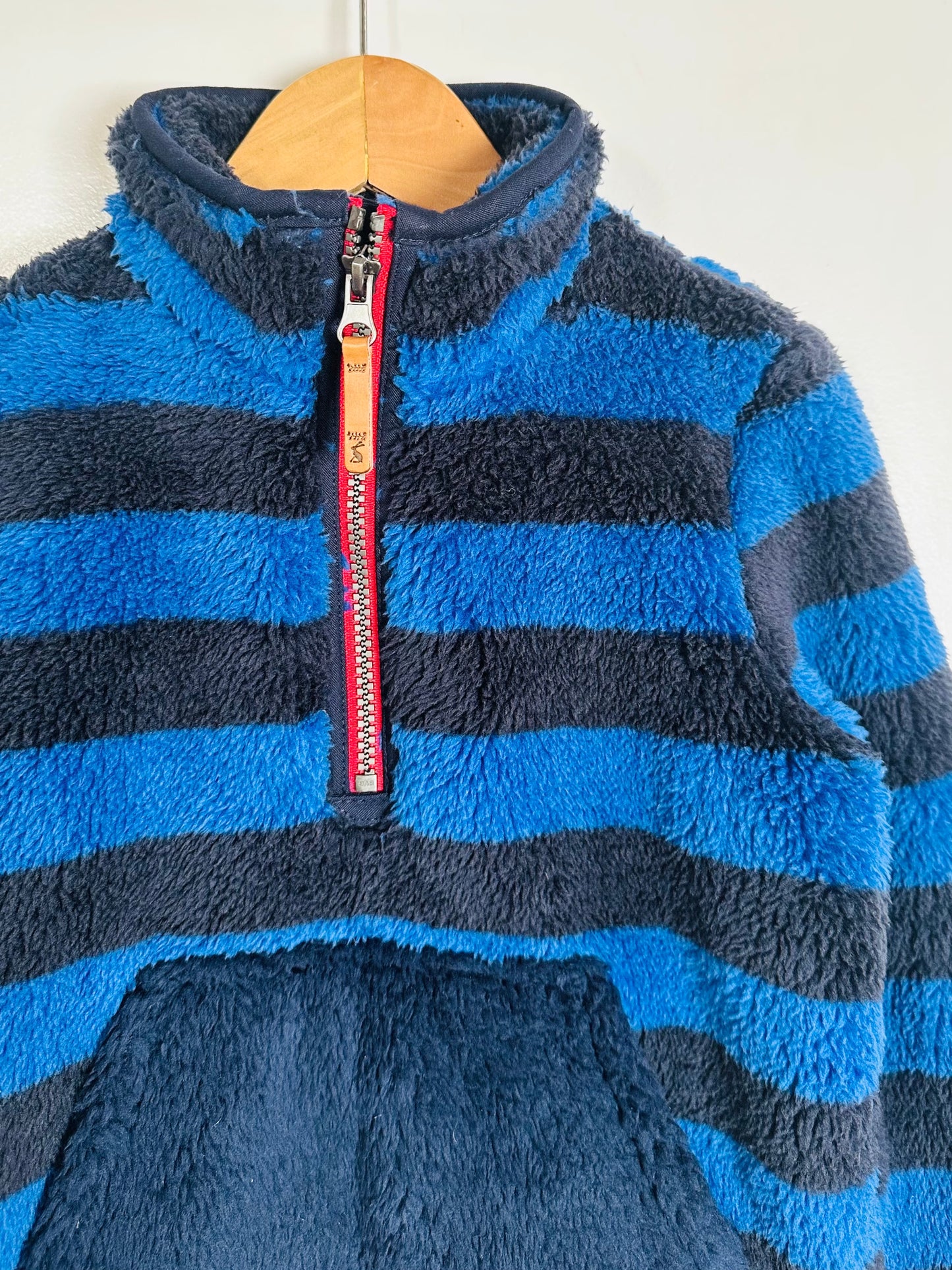 Blue striped fleece pullover with a red zipper on a wooden hanger.