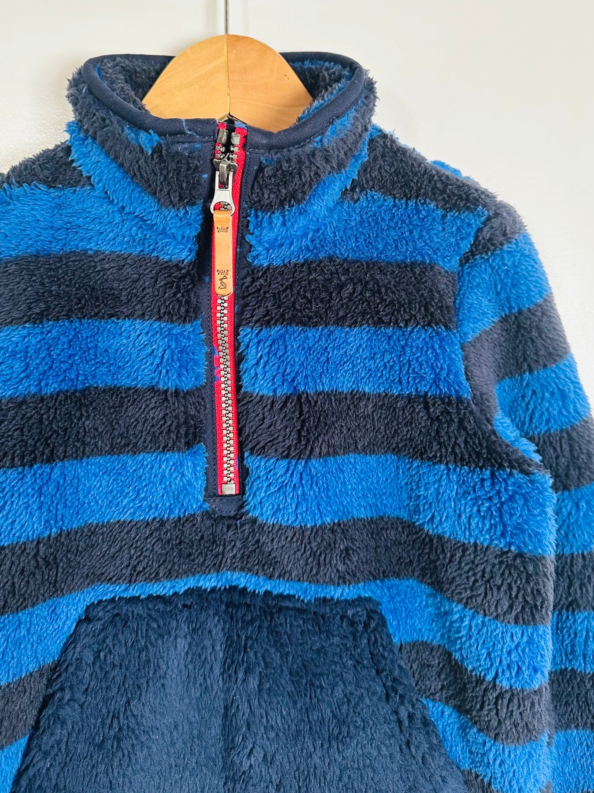 Blue striped fleece pullover with a red zipper on a wooden hanger.