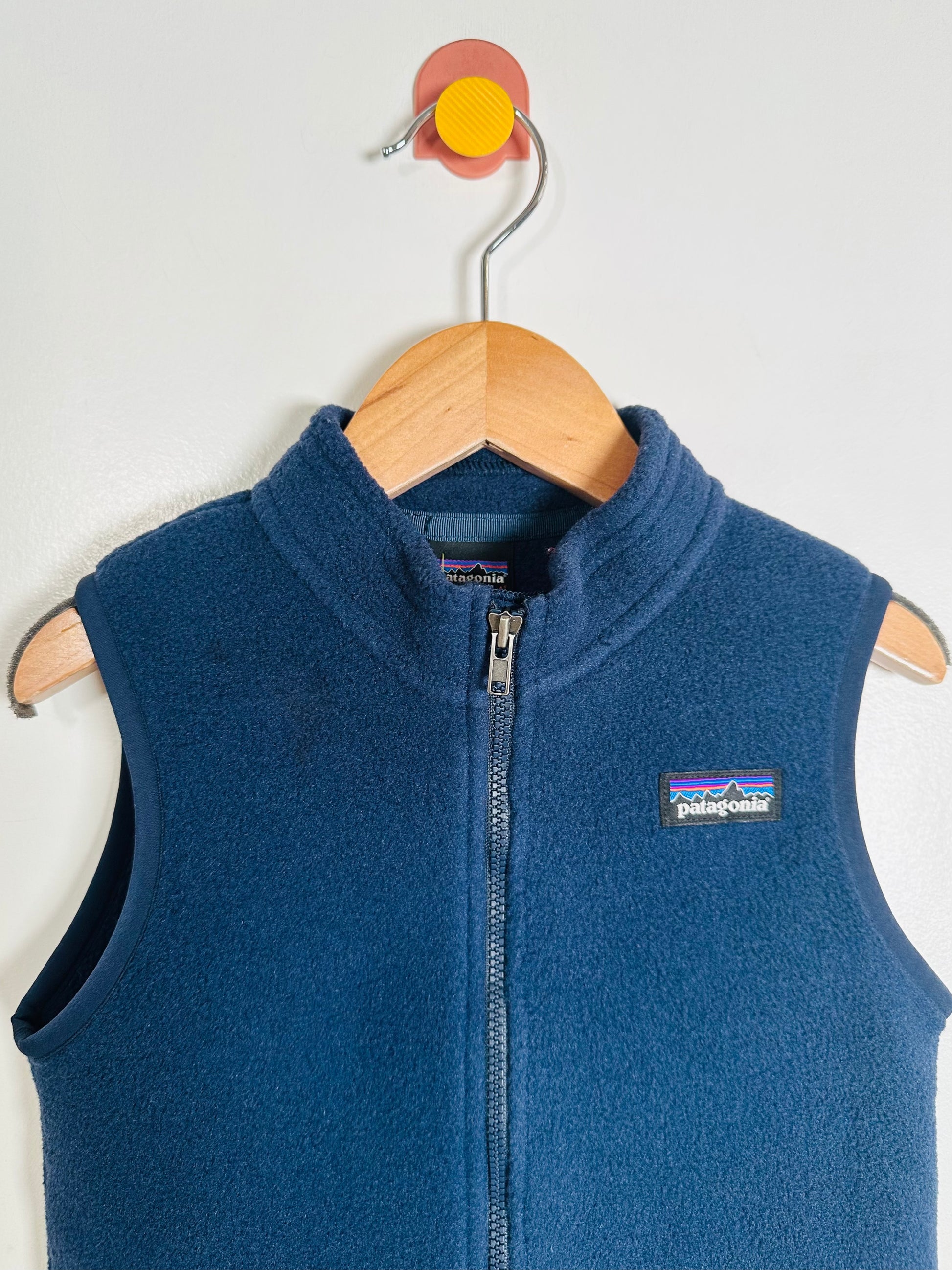 Blue vest with Patagonia logo on a wooden hanger against a white background