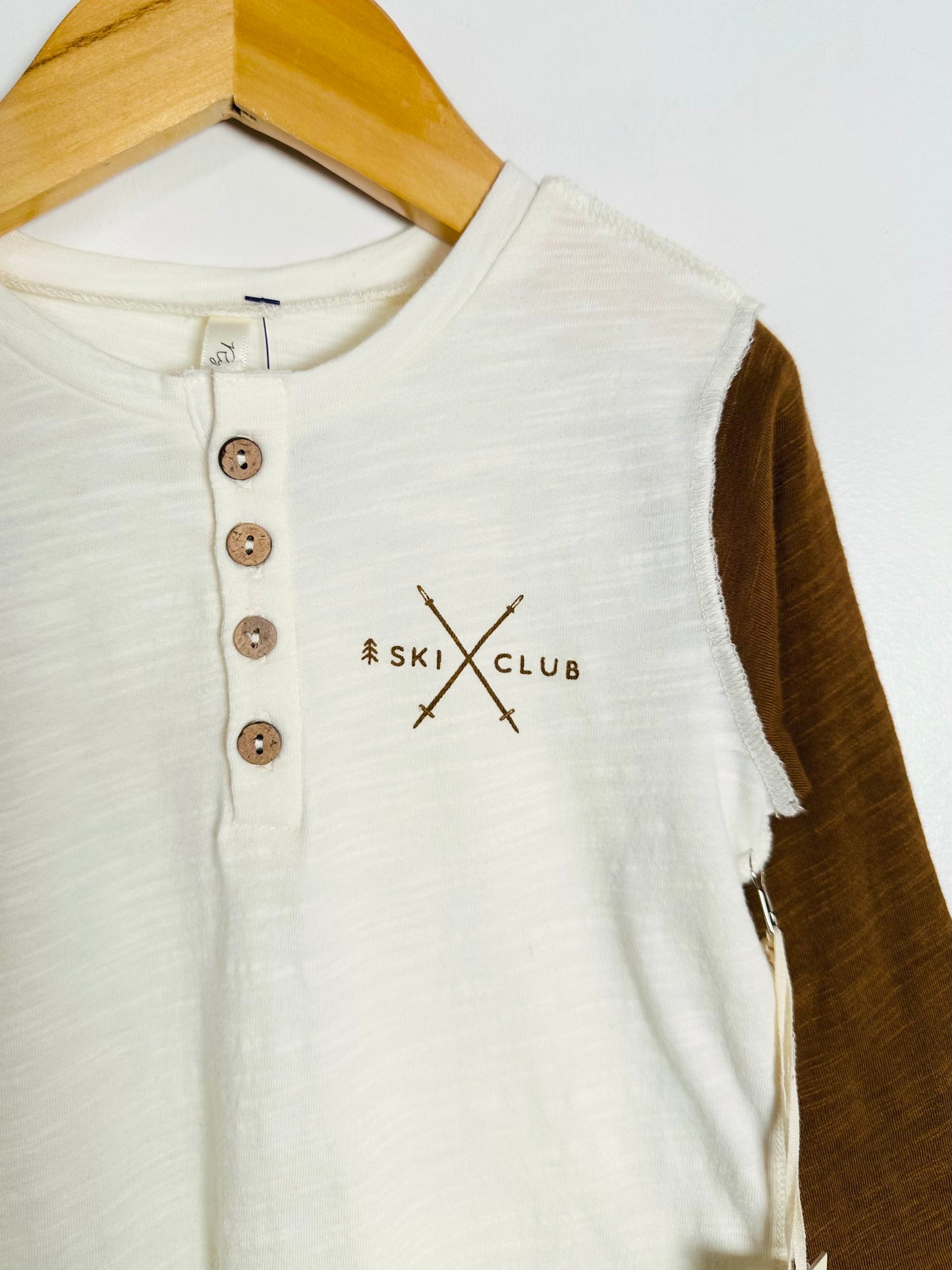 White and brown shirt with 'Ski Club' logo on a hanger