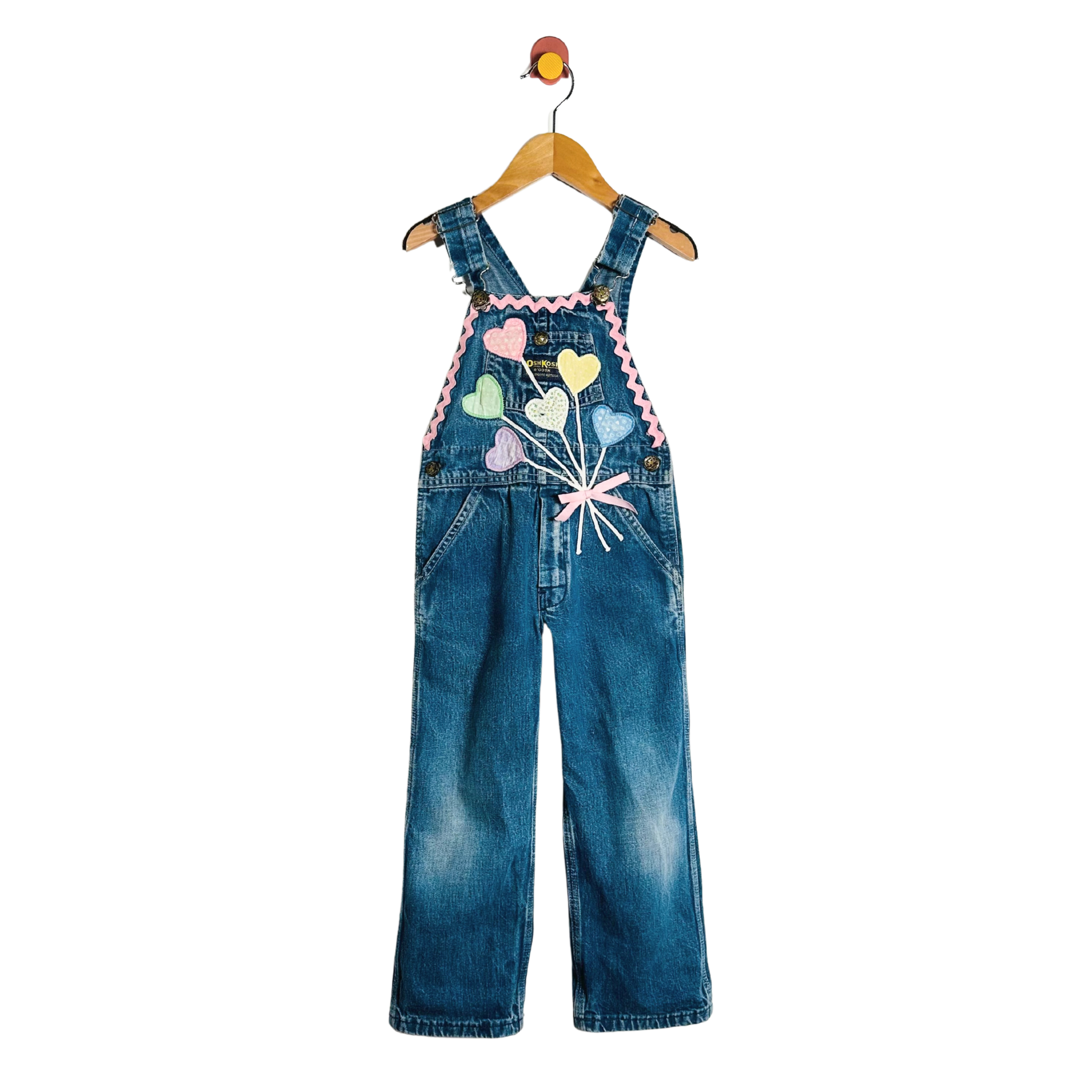 Children's denim overalls with colorful heart design on a hanger against a white background