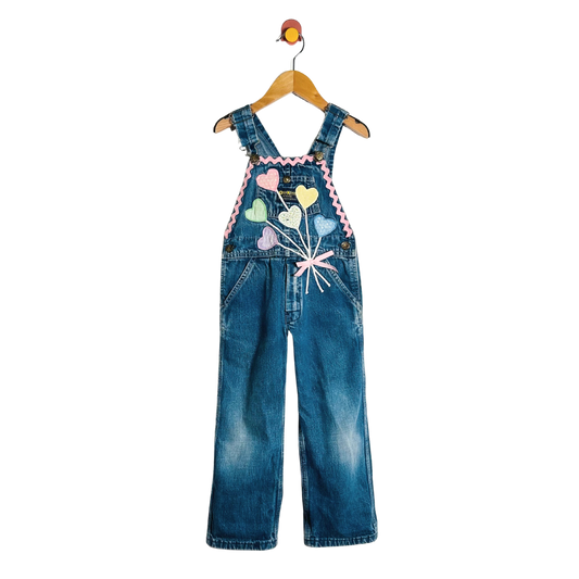 Children's denim overalls with colorful heart design on a hanger against a white background