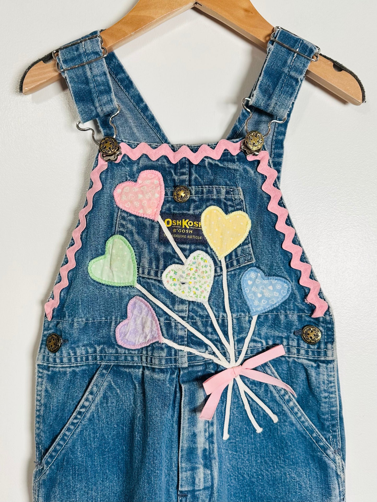 Denim overalls with heart-shaped balloons and ribbons on a white background
