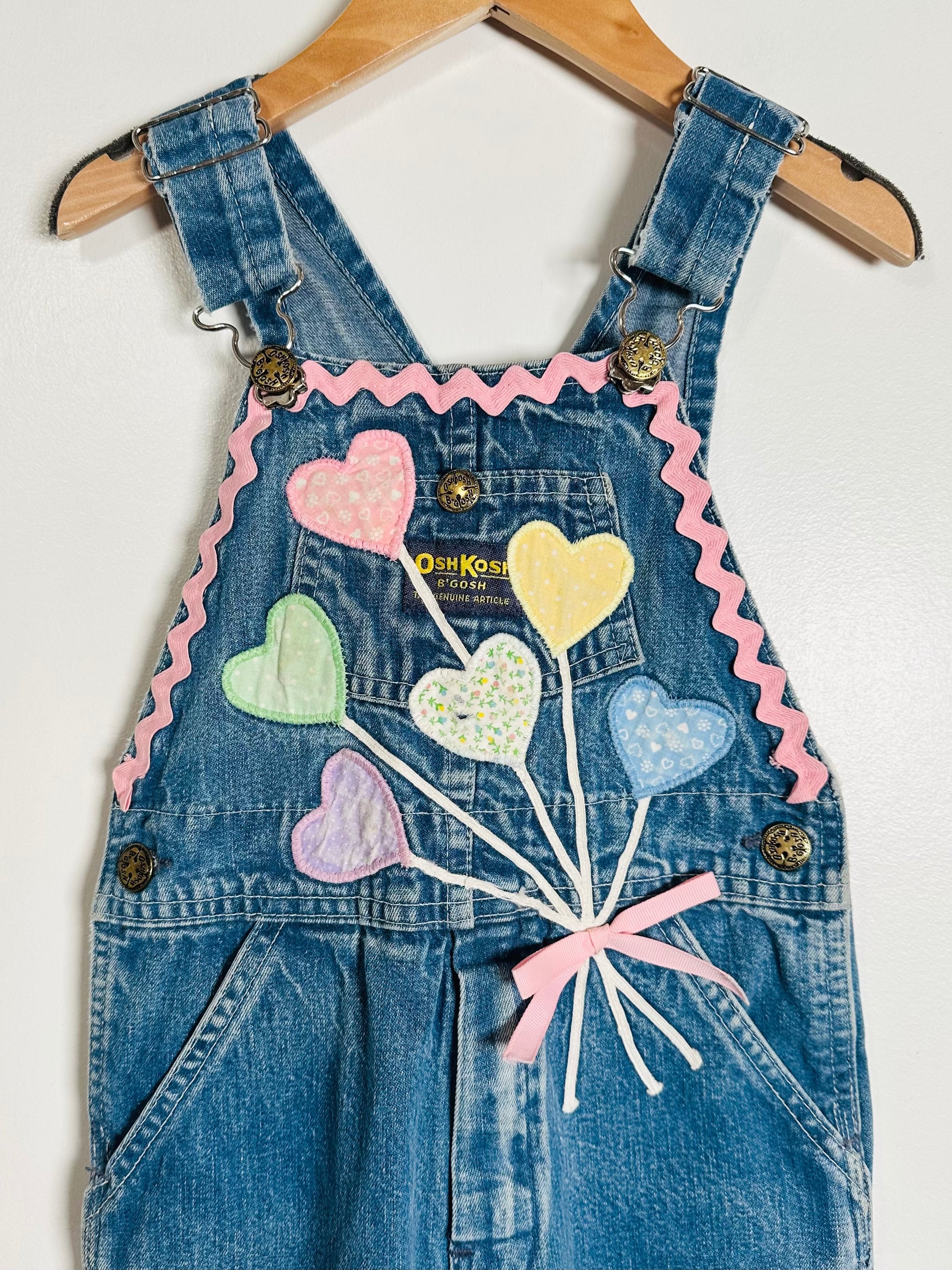 Denim overalls with heart-shaped balloons and ribbons on a white background