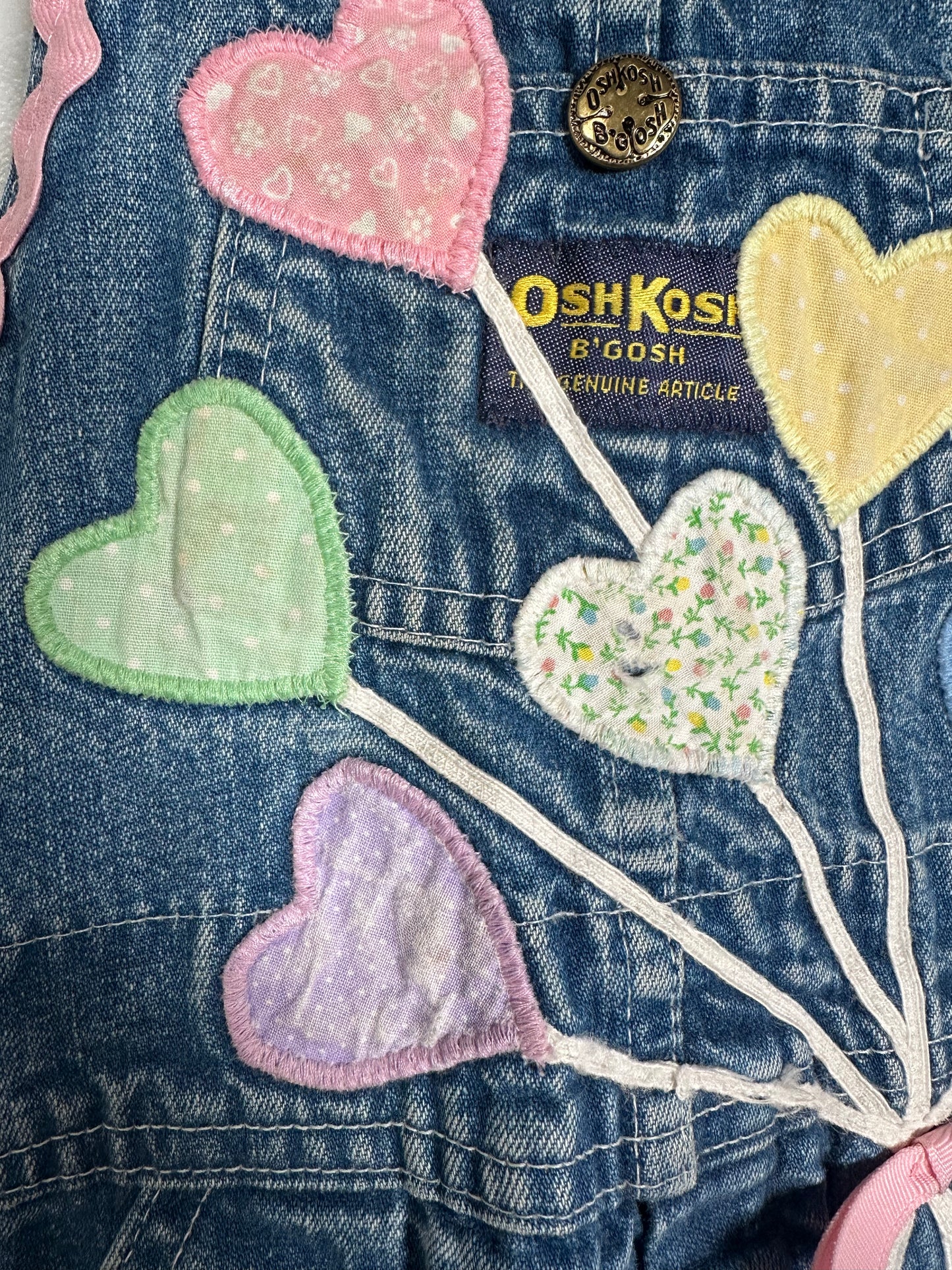 Denim overalls with colorful heart-shaped patches and OshKosh branding.