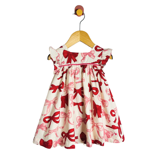 Children's dress with red and pink bow pattern on a hanger against a white background