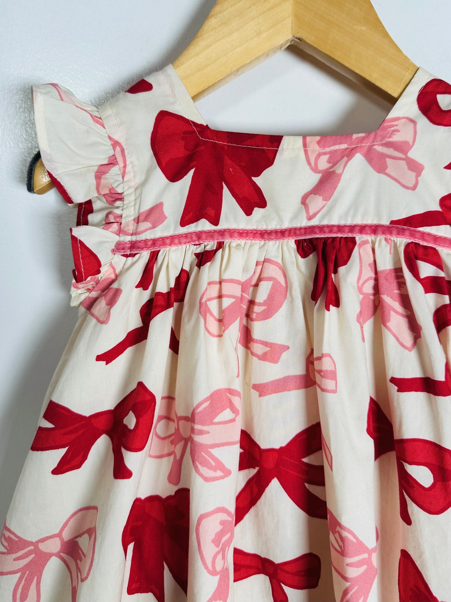 Children's dress with red and pink bow pattern on a hanger
