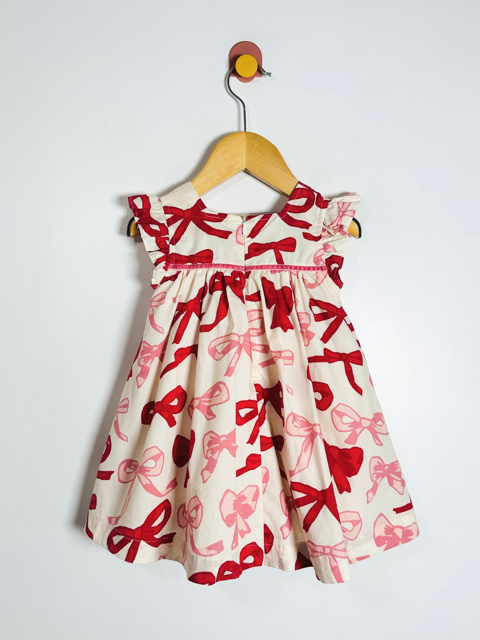 White dress with red bow pattern on a hanger against a white background