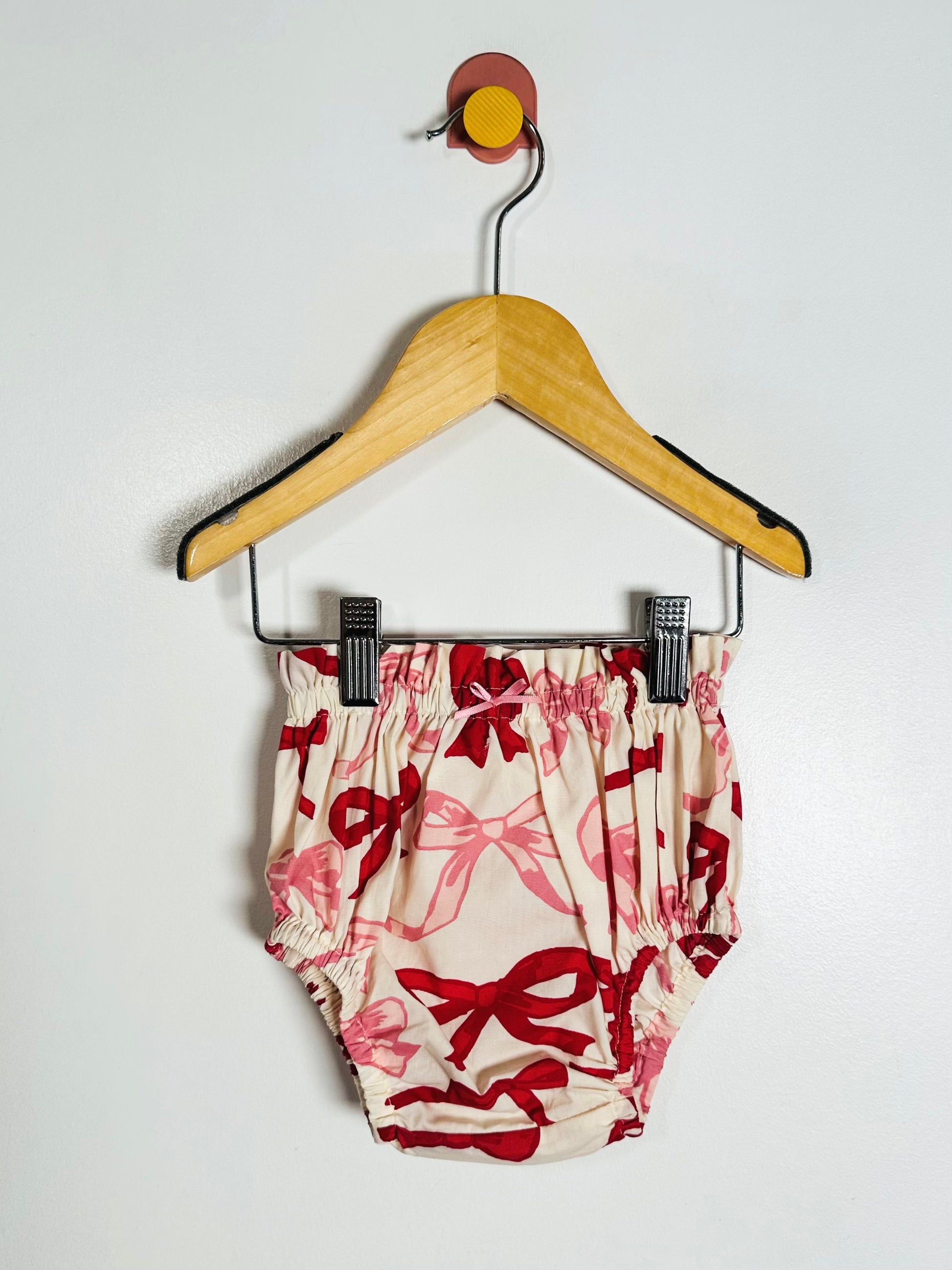 Baby bloomers with red floral pattern on a hanger against a white background