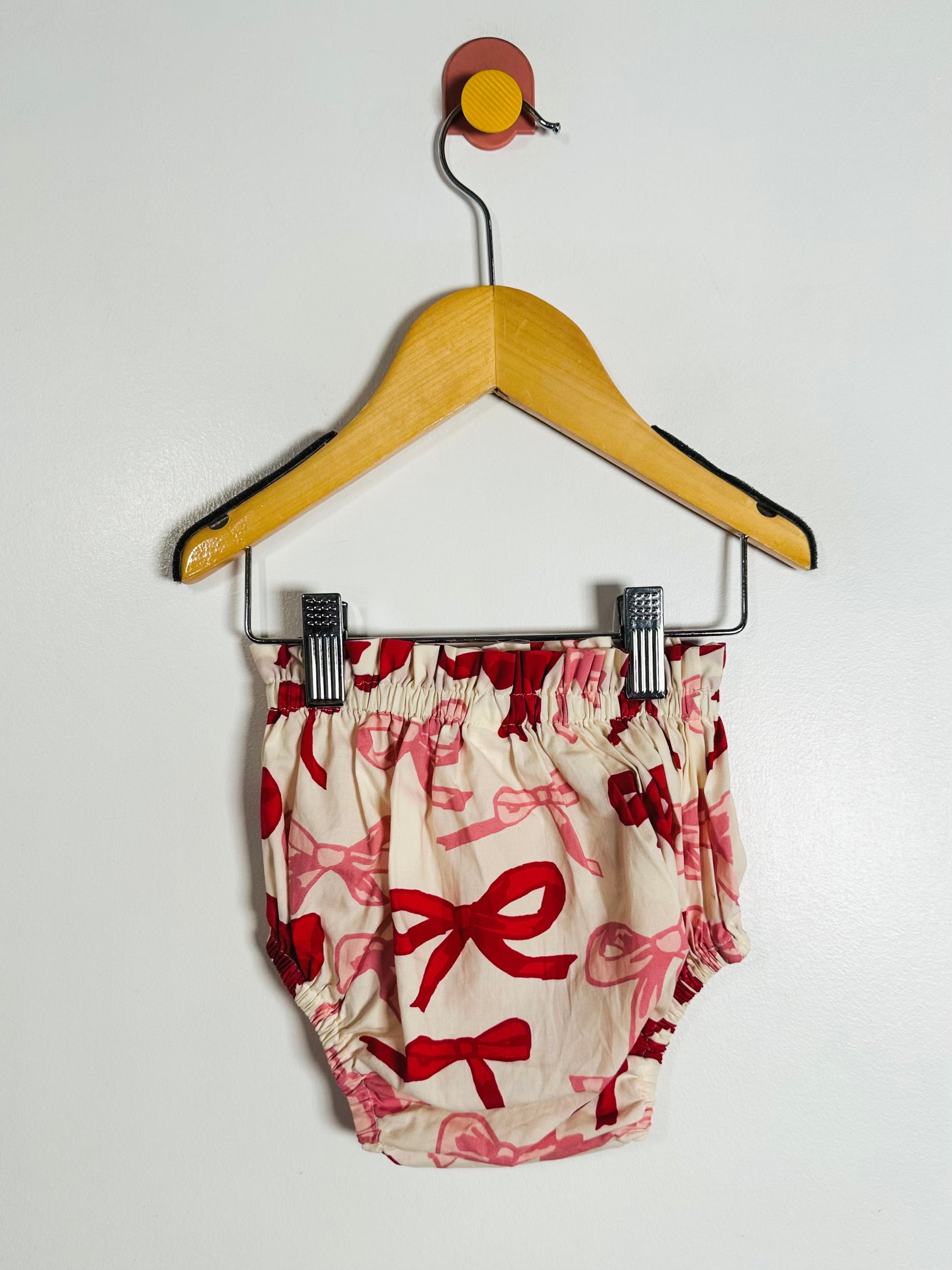 Baby bloomers with red bow pattern on a hanger against a white background
