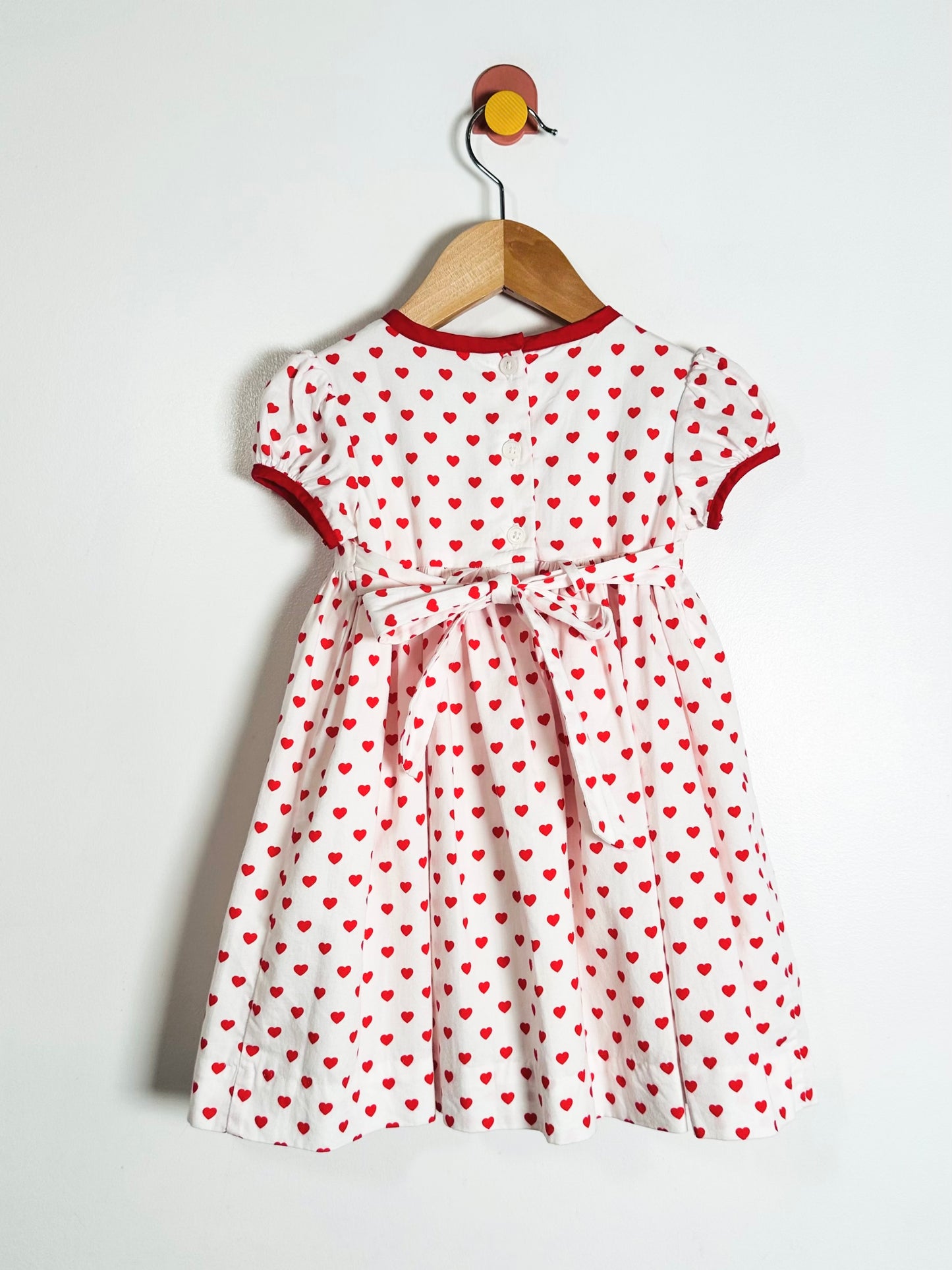 White dress with red heart pattern on a hanger against a white background