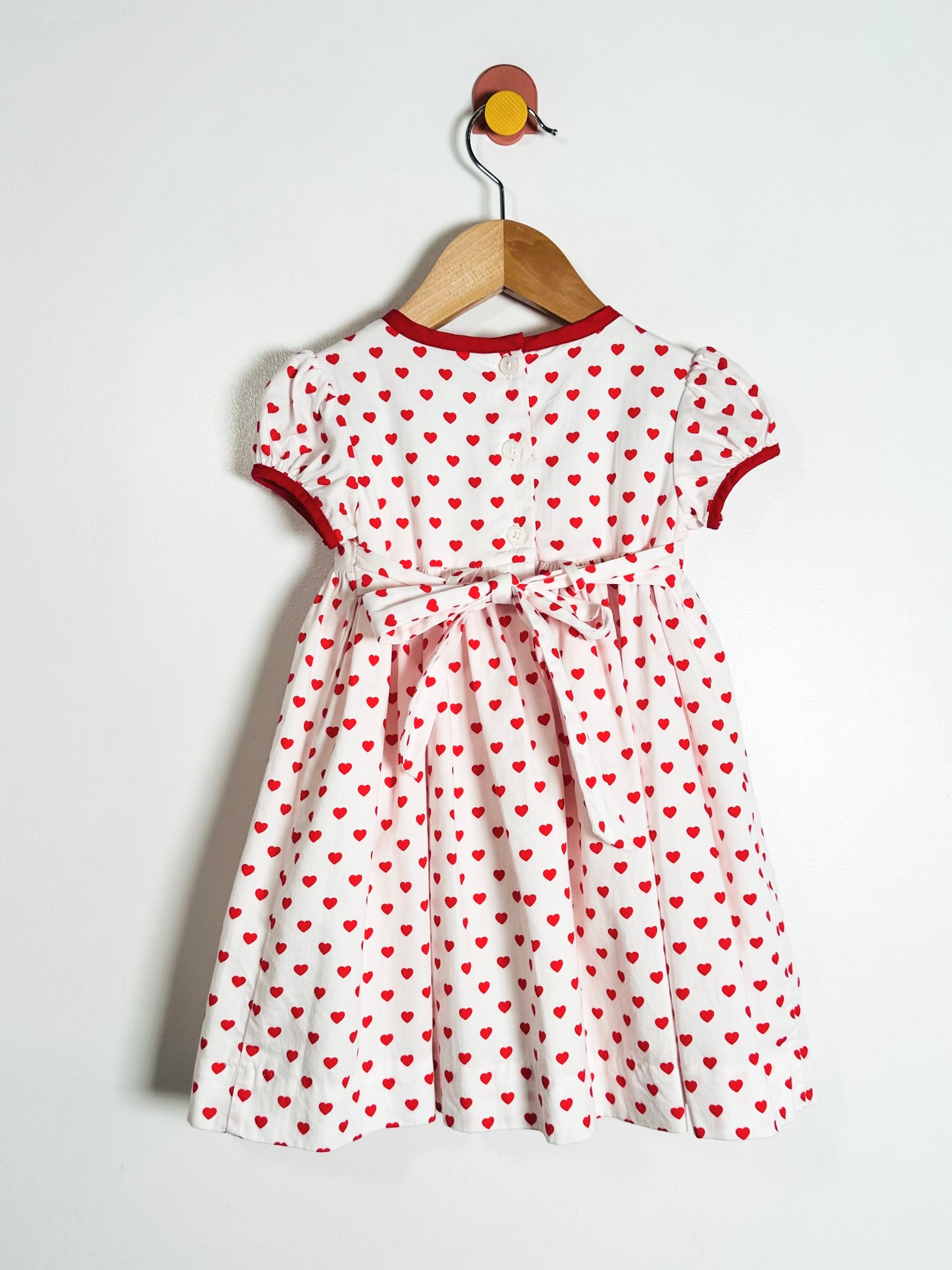 White dress with red heart pattern on a hanger against a white background