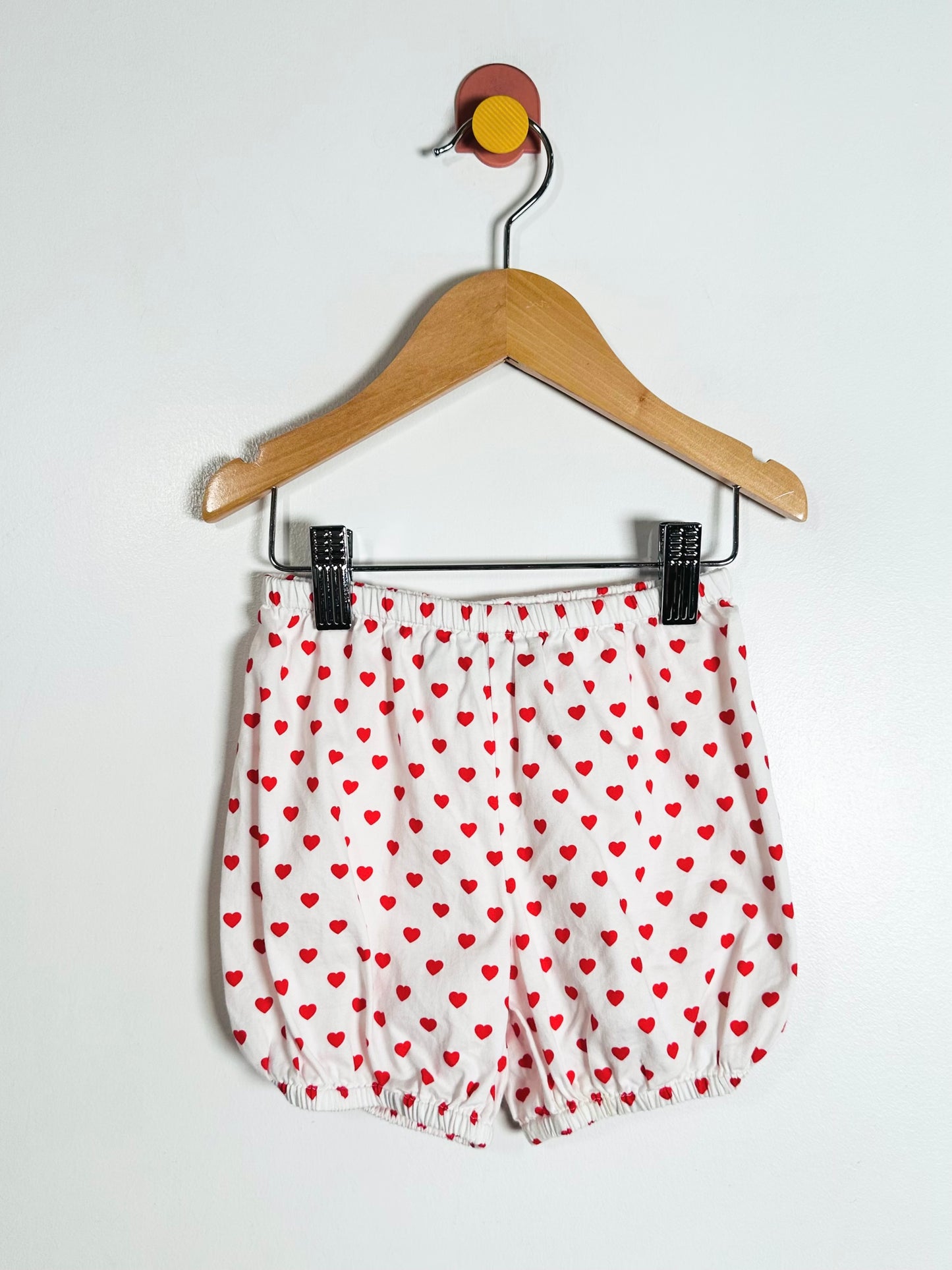 White shorts with red heart pattern on a hanger against a white background