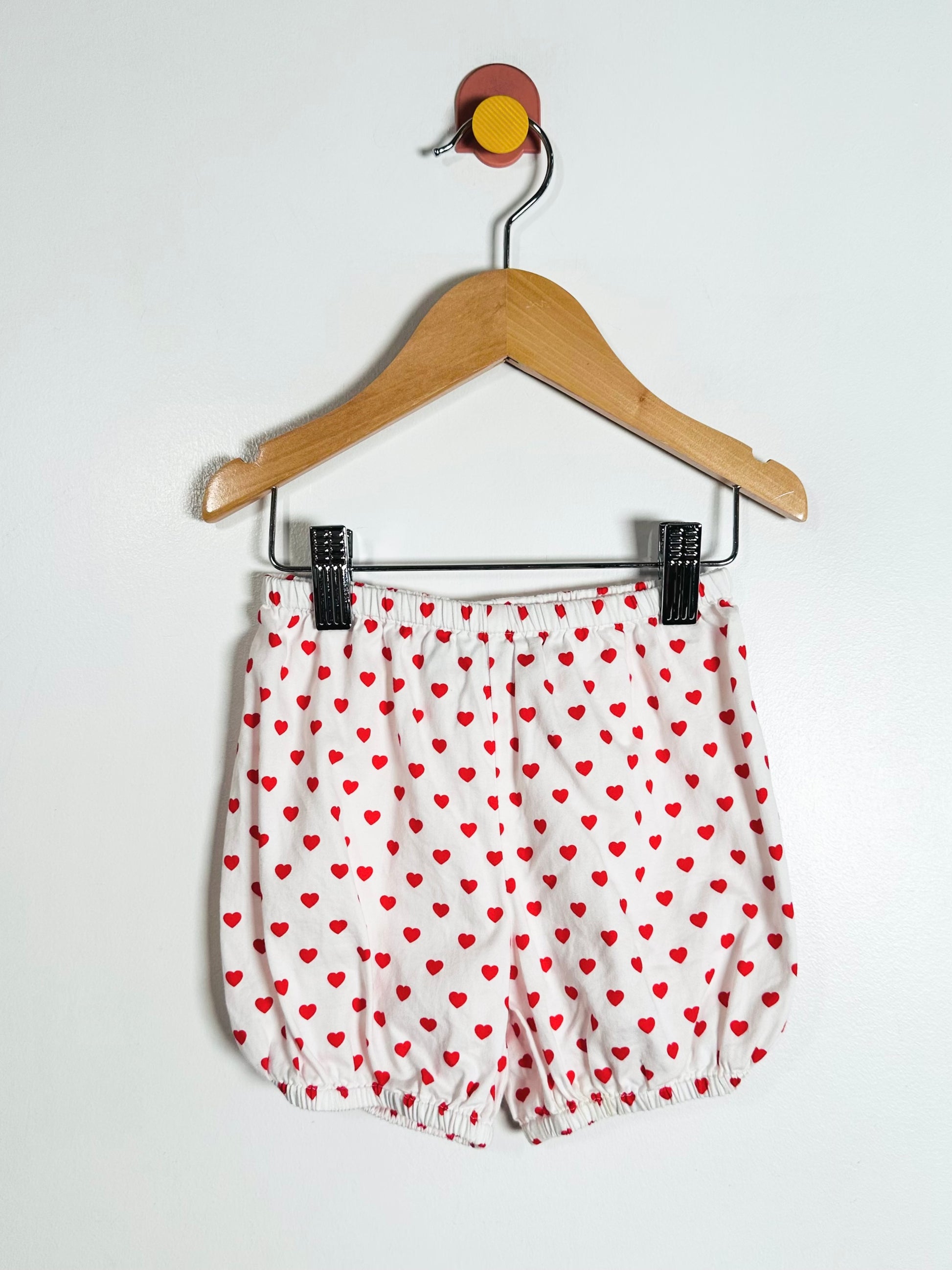 White shorts with red heart pattern on a hanger against a white background
