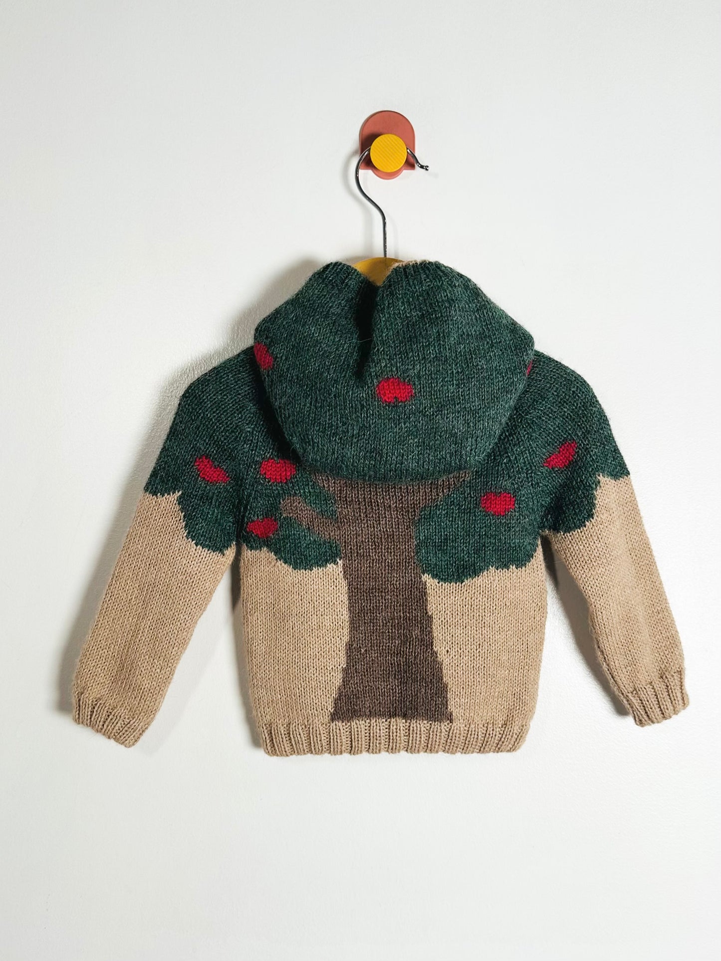 Children's sweater with tree design on a hanger against a white background