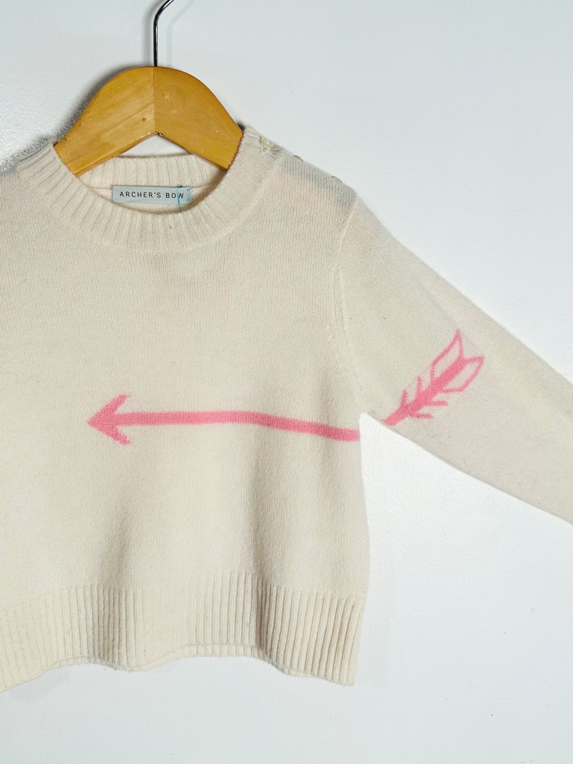 Beige sweater with pink arrow design on a hanger against a white background