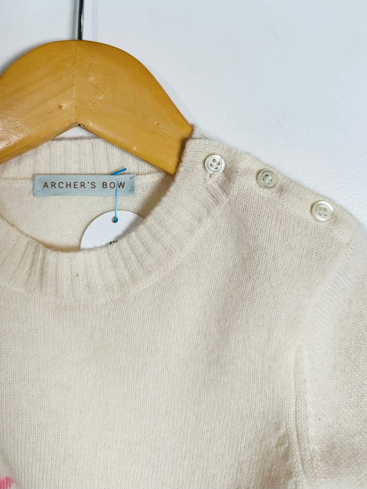 Beige baby sweater with buttons on a wooden hanger against a white background
