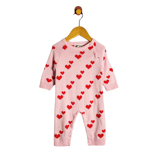 Pink baby romper with red heart patterns on a hanger against a white background